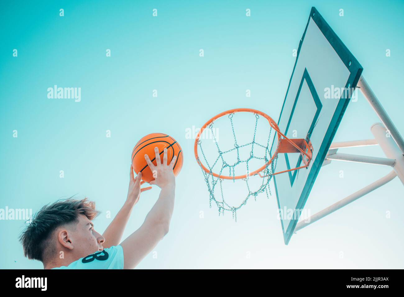 A low angle of a young Caucasian male dunking a basketball into the hoop Stock Photo