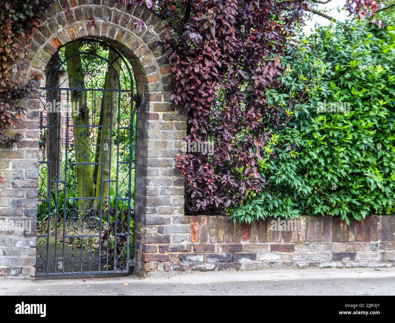 An arched wrought iron gate provides entry to a private garden in Harmondsworth, Hillingdon, Middlesex, London, England, UK. Stock Photo