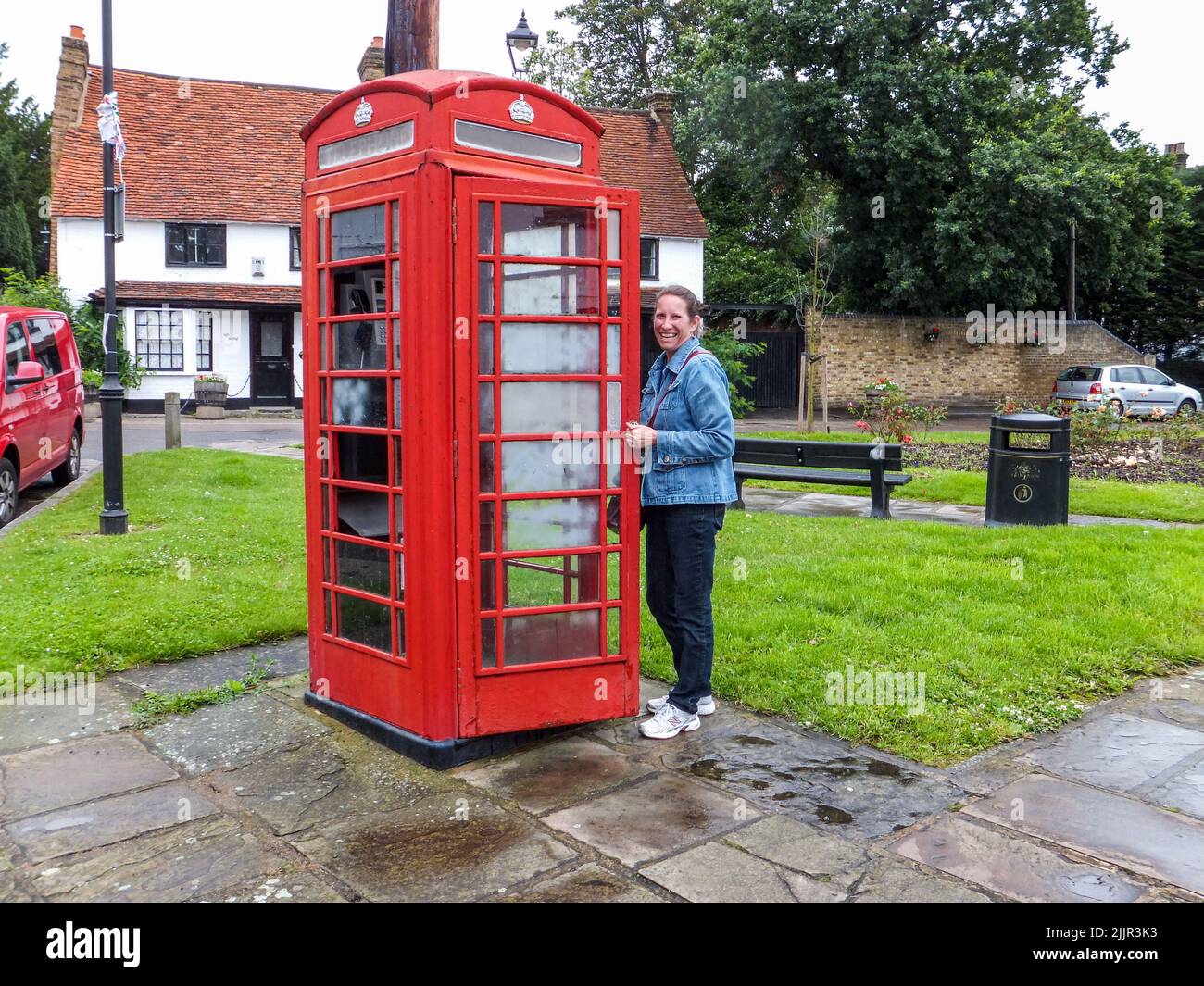 A woman opens the door and is about to enter an iconic red telephone booth in Harmondsworth, Hillingdon, Middlesex, London, England, UK. Stock Photo