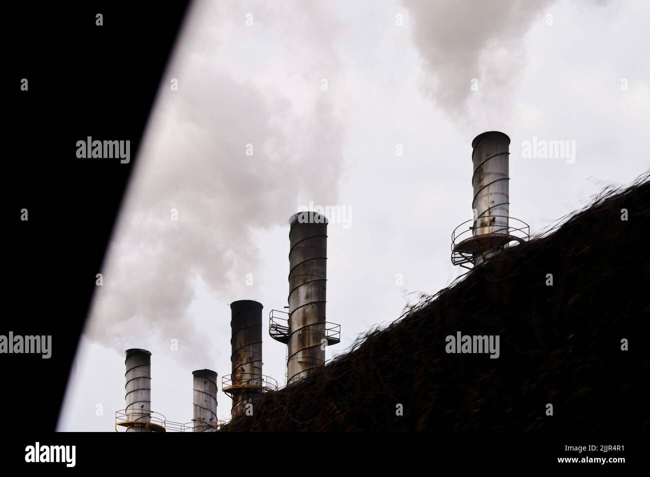 industrial smokestacks belching out smoke polluting behind a fence Stock Photo