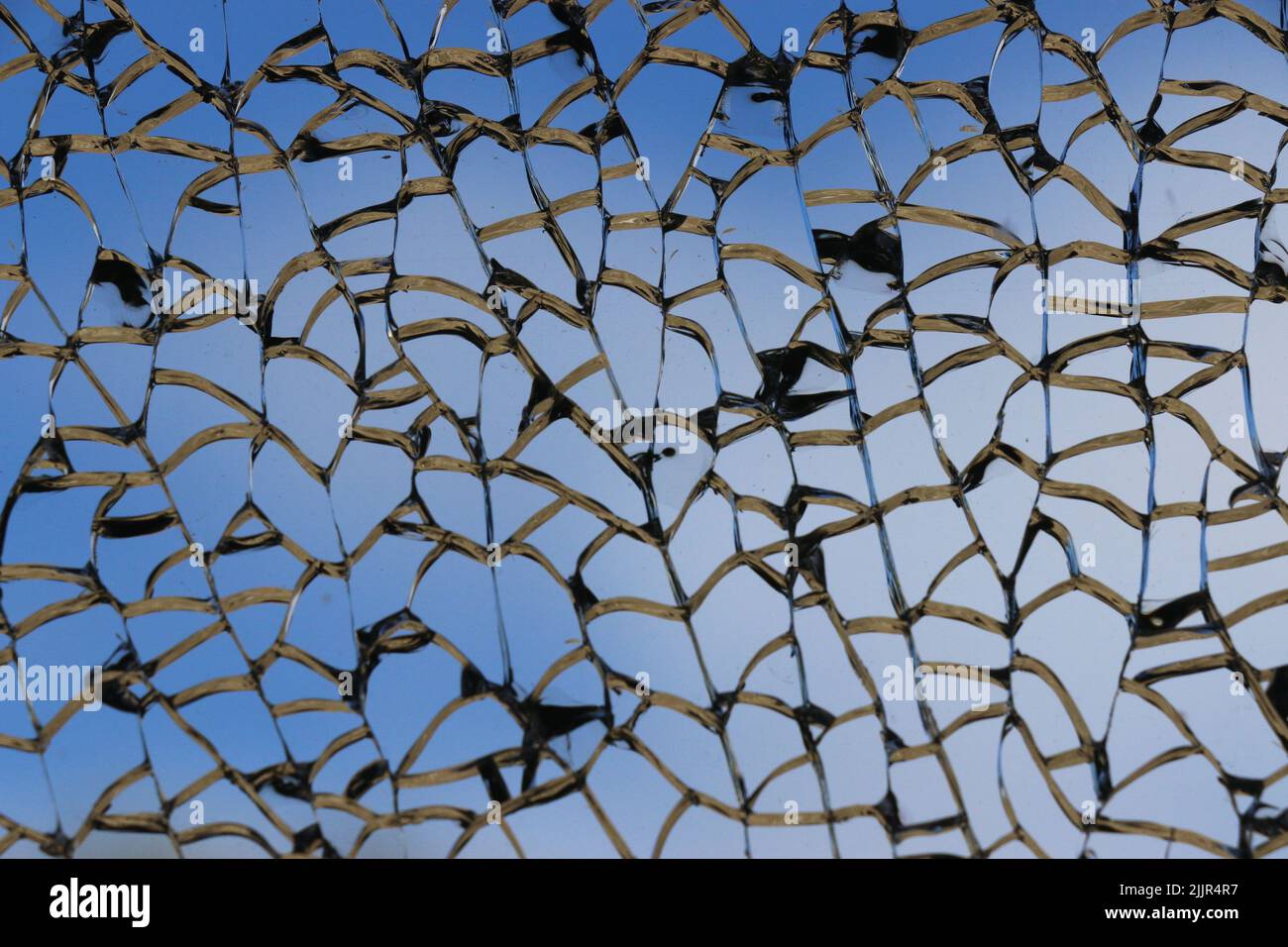 Beautiful silver lines of a shattered window create an intricate pattern against a deep blue sky. Stock Photo