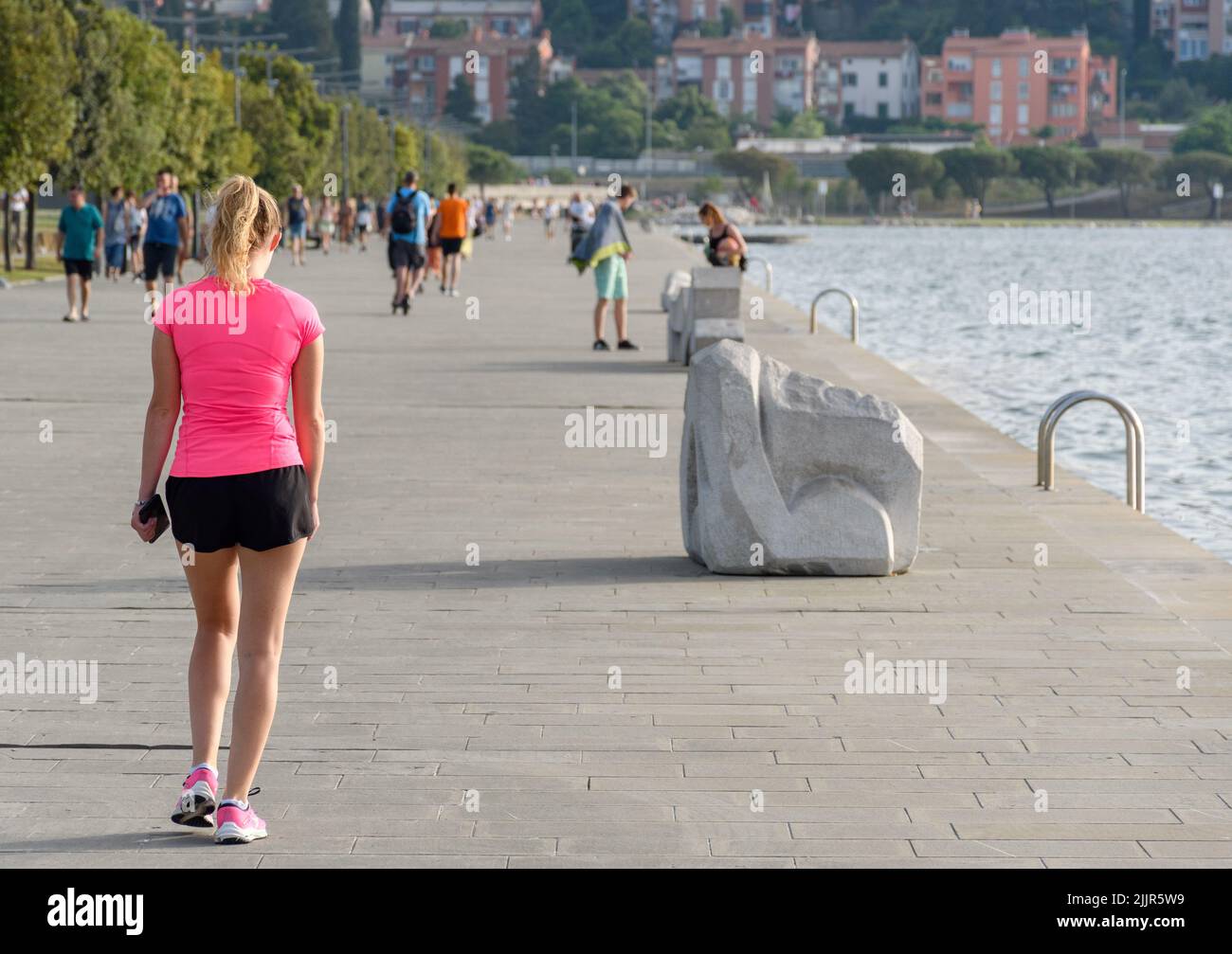 The Woman wearing pink sports top and shorts, walking on the waterfront ...