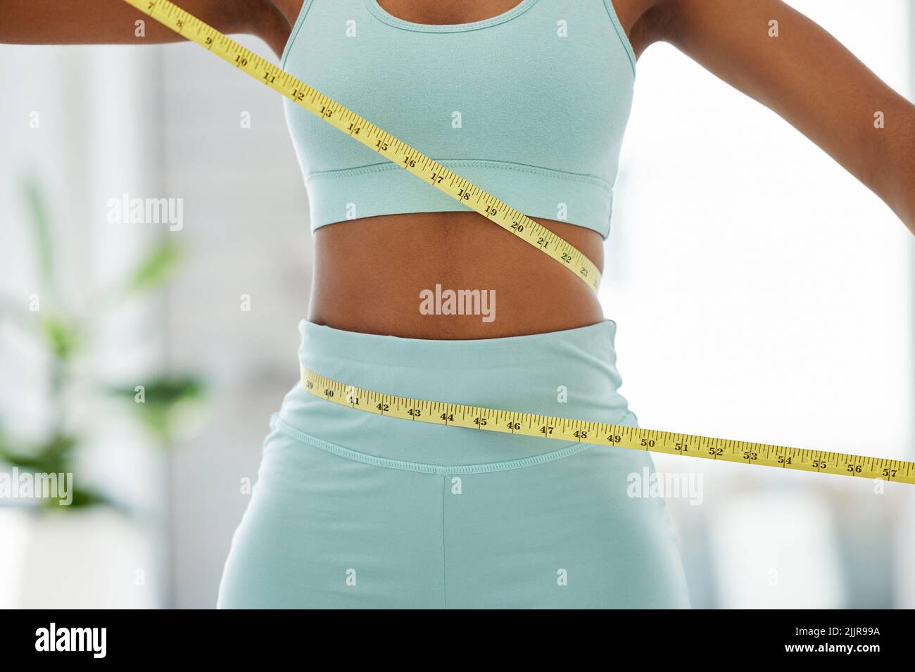https://c8.alamy.com/comp/2JJR99A/losing-those-pounds-an-unrecognisable-woman-standing-alone-and-using-a-measuring-tape-around-her-waist-in-a-yoga-studio-2JJR99A.jpg