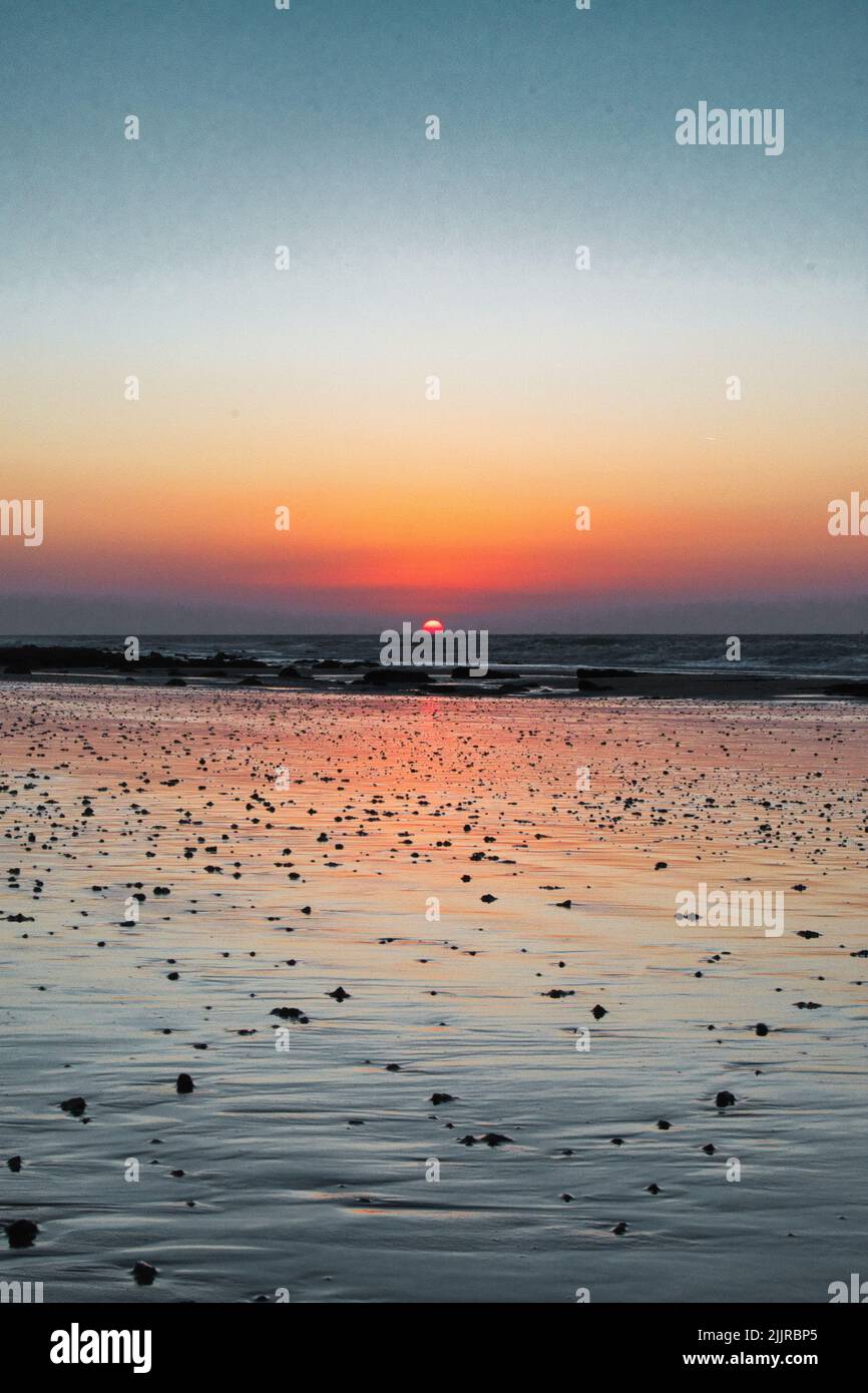 A vertical of the sun setting and reflecting on the surface of the sea ...