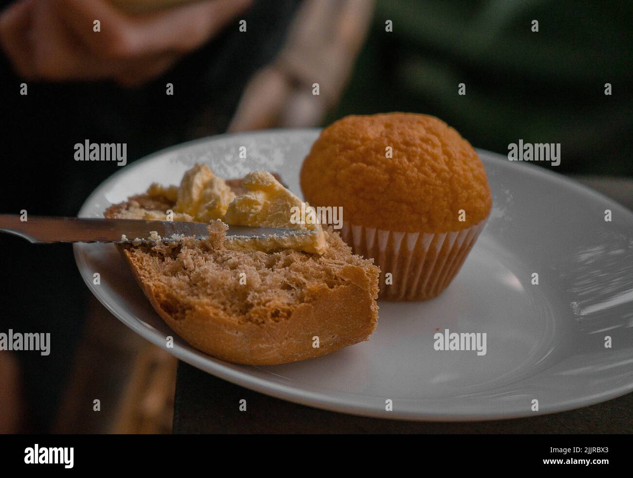 A white plate with a muffin and small sandwich with butter on a blurry background Stock Photo