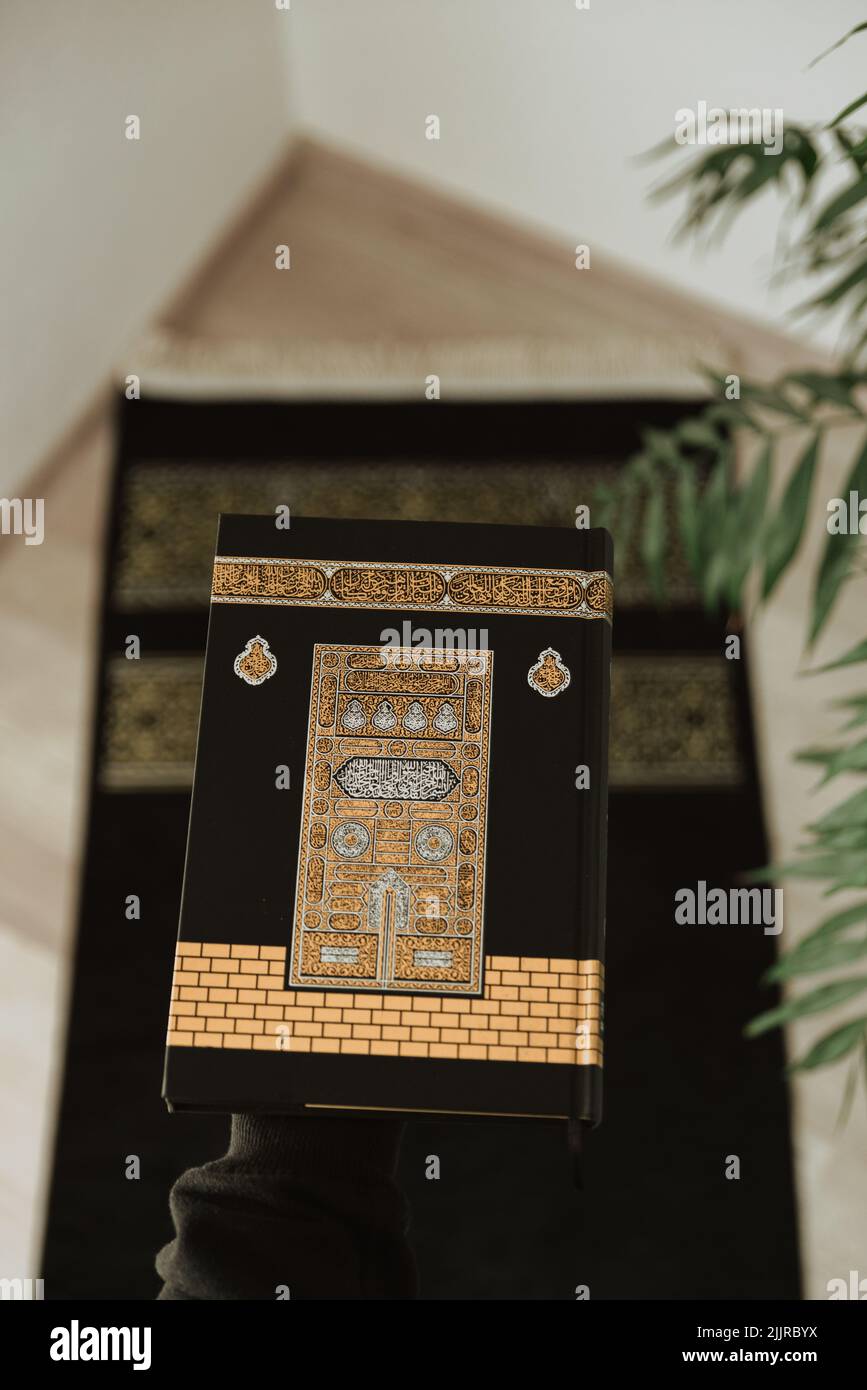 A vertical shot of a black rug and a black velvet Quran decorated with a Kaaba pattern. Stock Photo