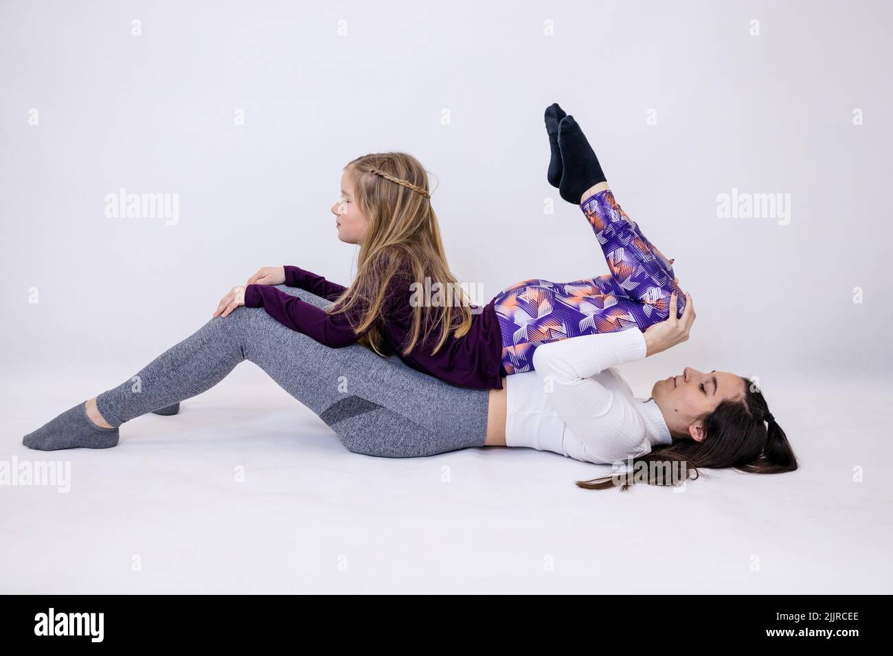 Young attractive yoga teacher and her little student doing performing intensive movements while exercising Stock Photo