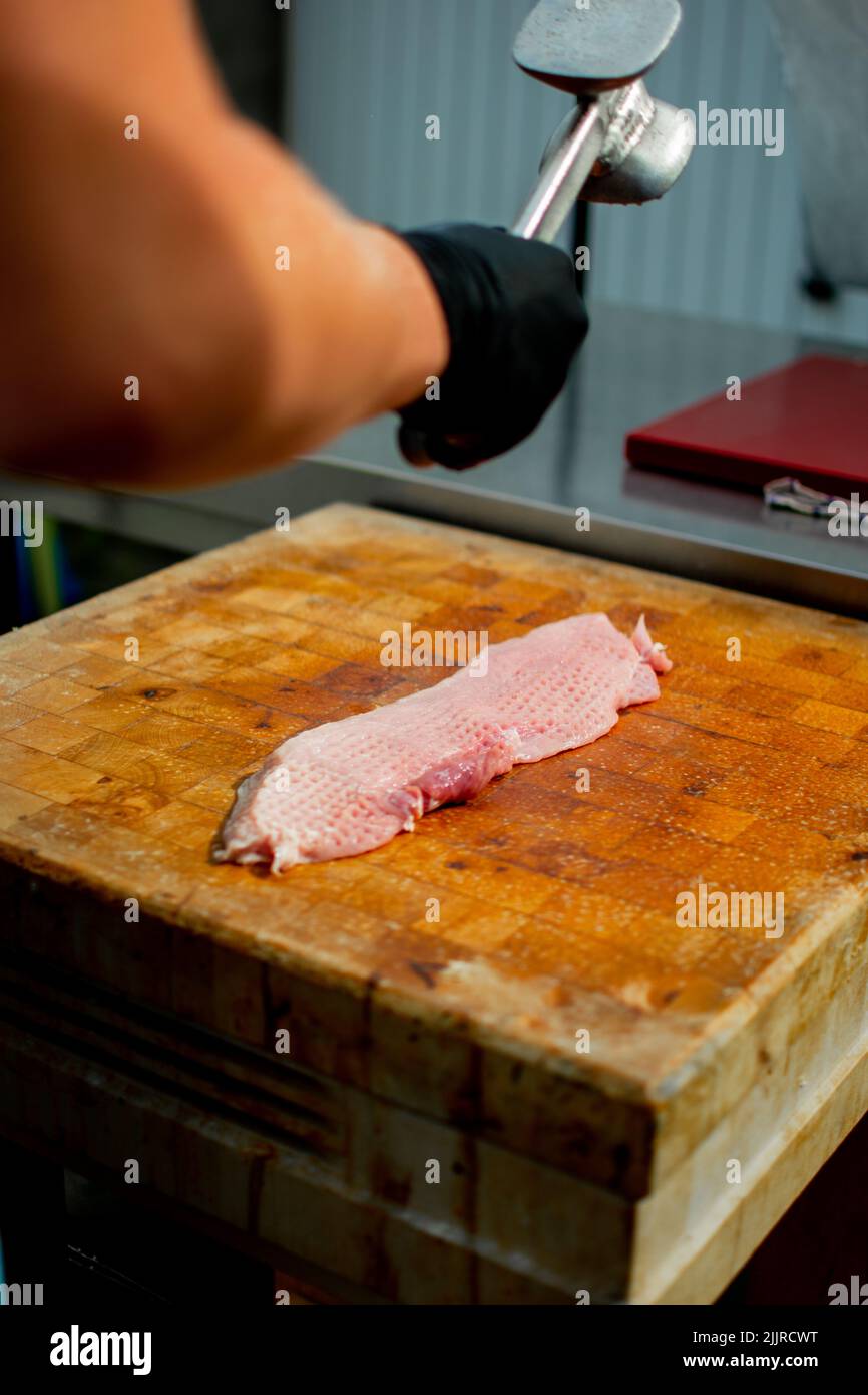 A vertical shot of a person tenderizing a piece of meat Stock Photo