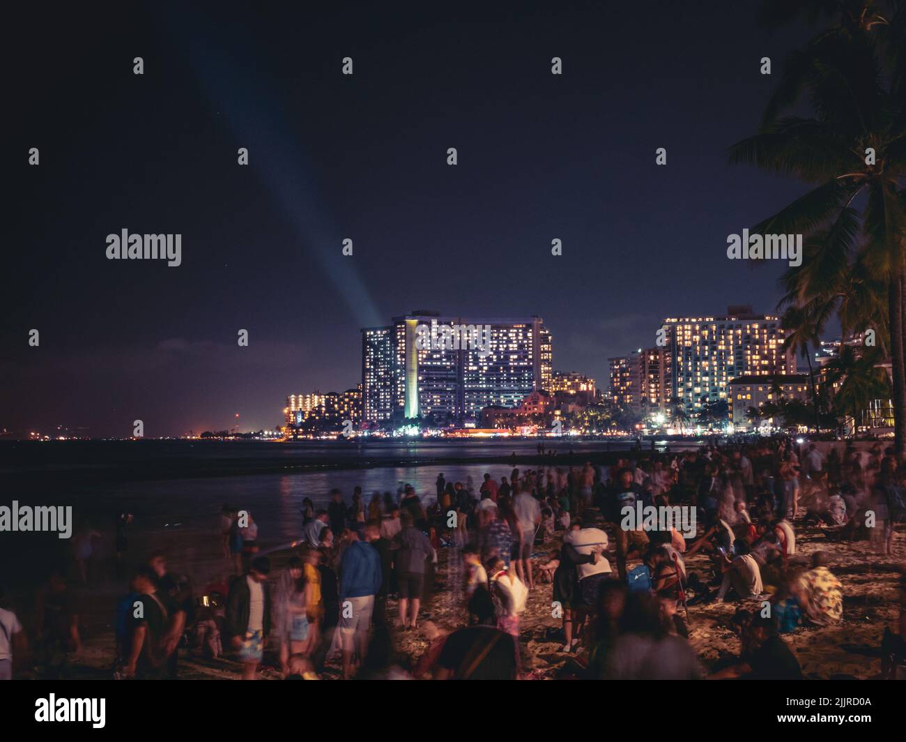 A coast full of people with illuminated buildings in the background at New Year Eve in Hawaii, Waikiki Stock Photo