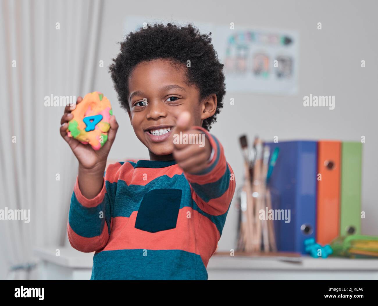 Im 4 years old. What about you. a young boy showing thumbs up while holding play dough. Stock Photo