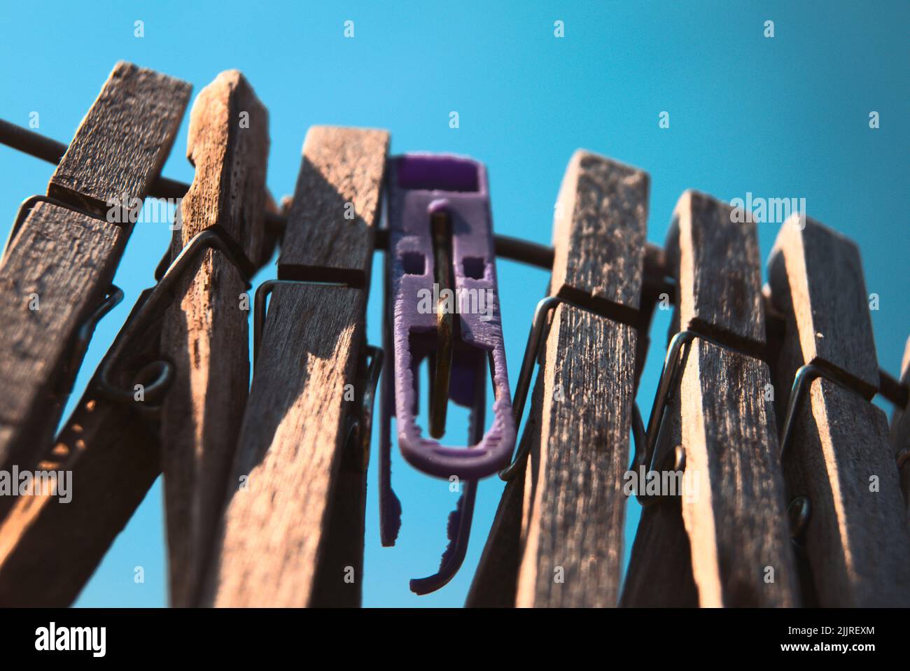 A closeup shot of wooden clothes pins hanging on rope against a blue sky Stock Photo