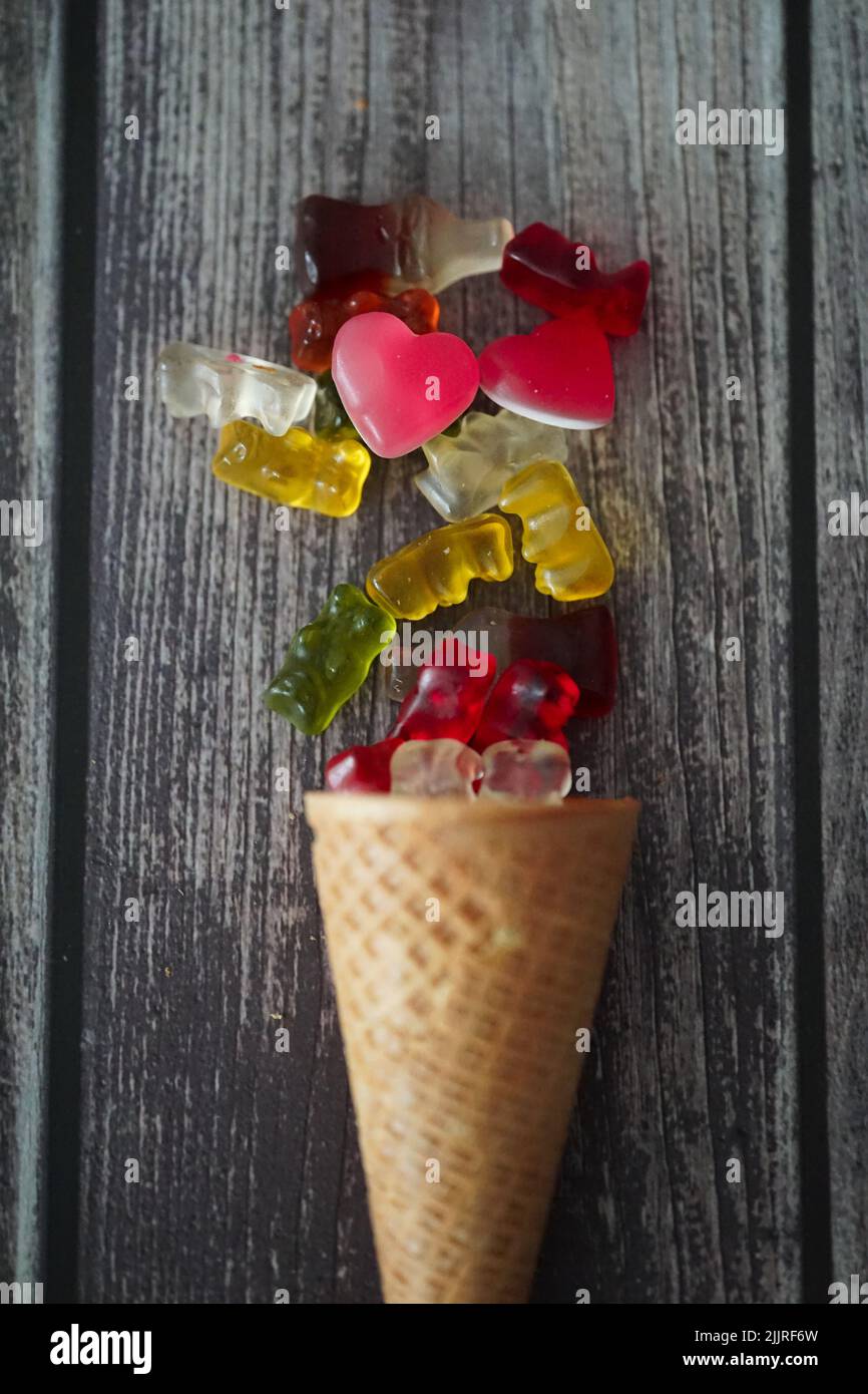 The colorful gummy bears and the hearts by the waffle cone on a wooden surface Stock Photo