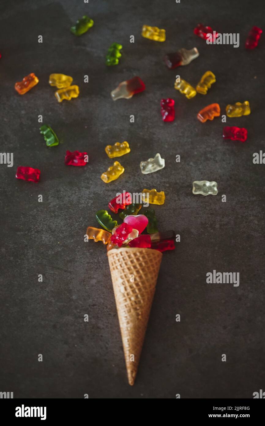 A vertical closeup shot of an ice cream cone with gummy bears on the dark surface Stock Photo