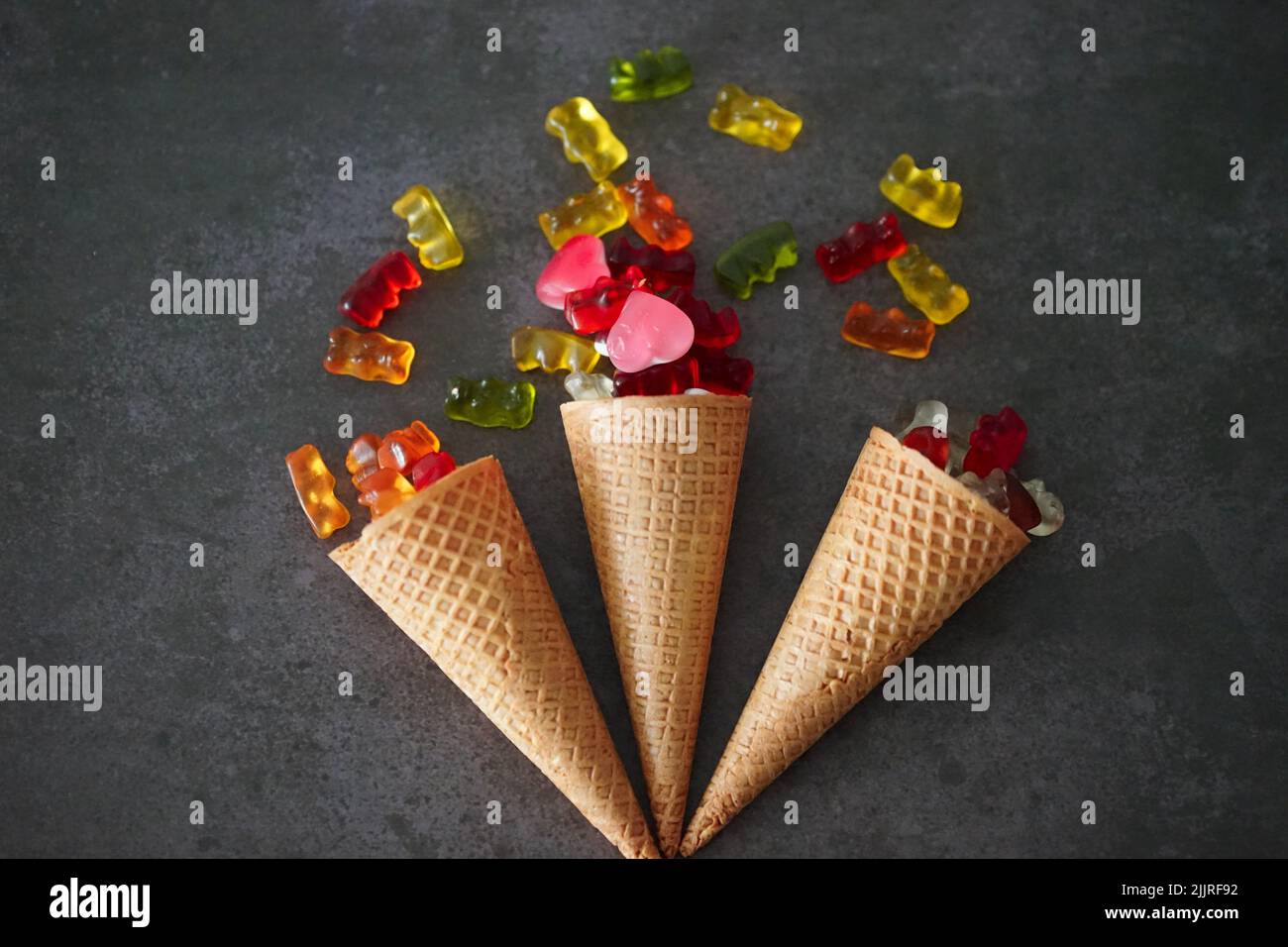 A closeup of three ice cream cones with gummy bears on the dark surface Stock Photo