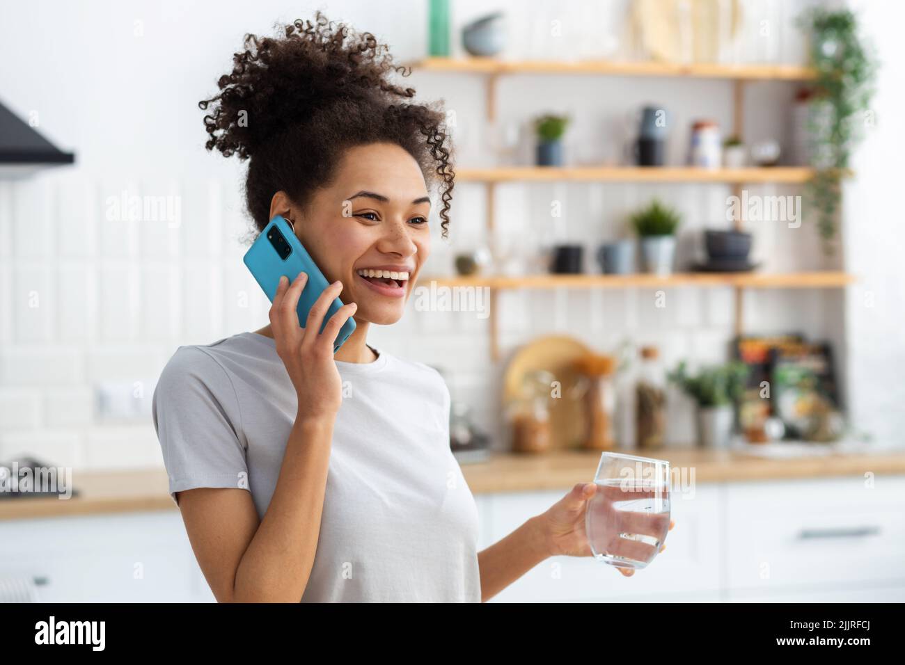 Smiling African American woman holding glass of clean water talking on mobile phone healthy lifestyle concept Stock Photo