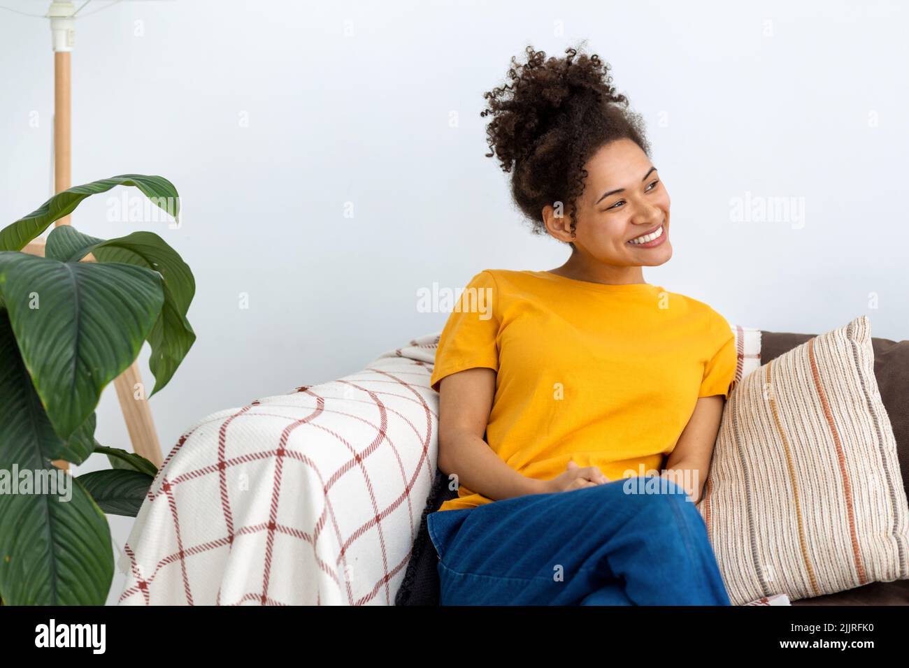 carefree woman relax sitting on a sofa at home, looking away and smiling friendly Stock Photo