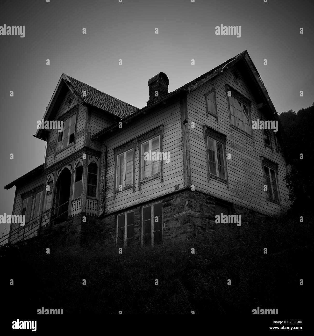 A low angle grayscale of an enormous abandoned ghost house with broken windows in Norway Stock