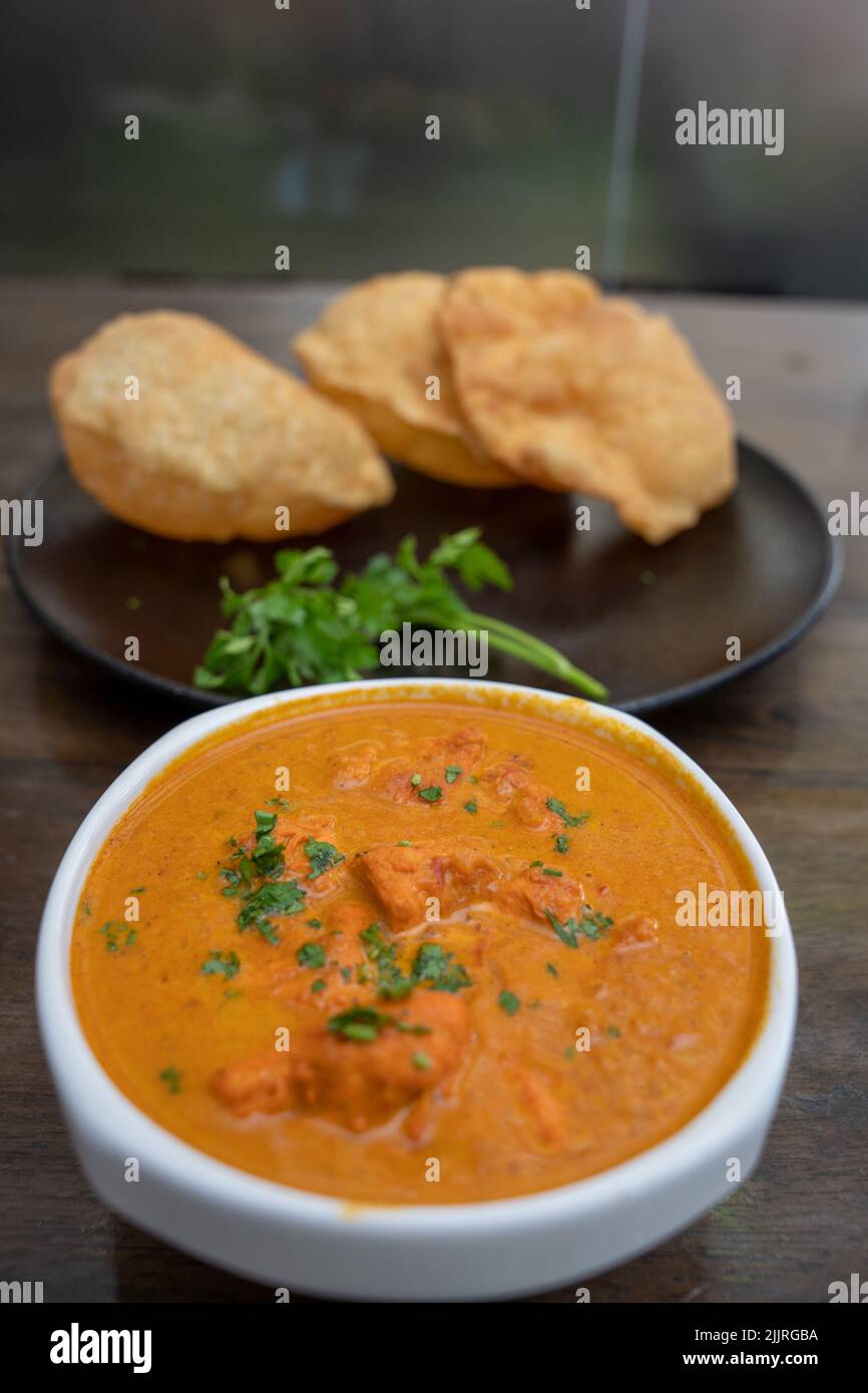 a Butter chicken served in selective focus with Homemade Indian Naan Bread blurred in the background, Murgh Makhani Stock Photo