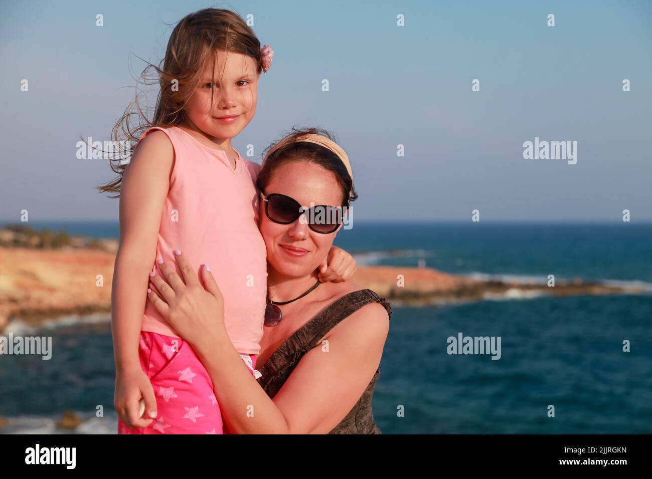 Happy mother with smiling little daughter are on a beach on a sunny day, real family outdoor portrait Stock Photo