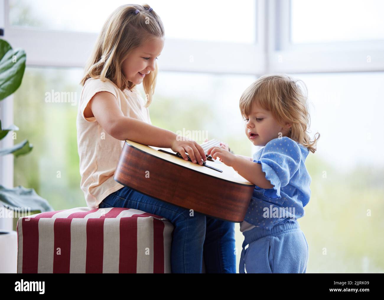 The best thing in the world is a big sister. two little sisters playing the guitar at home. Stock Photo