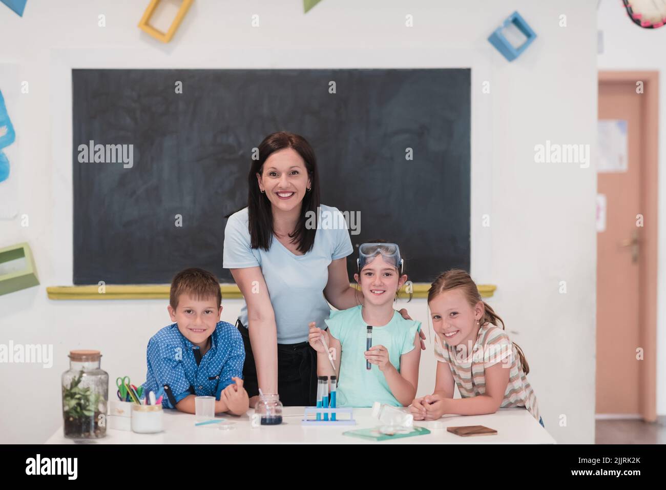 Elementary School Science Classroom: Enthusiastic Teacher Explains Chemistry to Diverse Group of Children, Little Boy Mixes Chemicals in Beakers Stock Photo