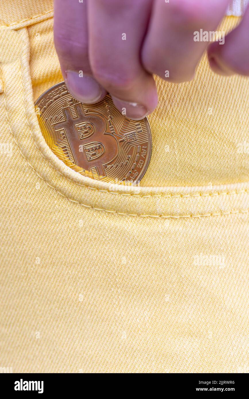 Close-up of woman putting bitcoin in yellow jeans pocket, golden cryptocurrency coin in pocket background, concept of digital currency virtual money. High quality photo Stock Photo