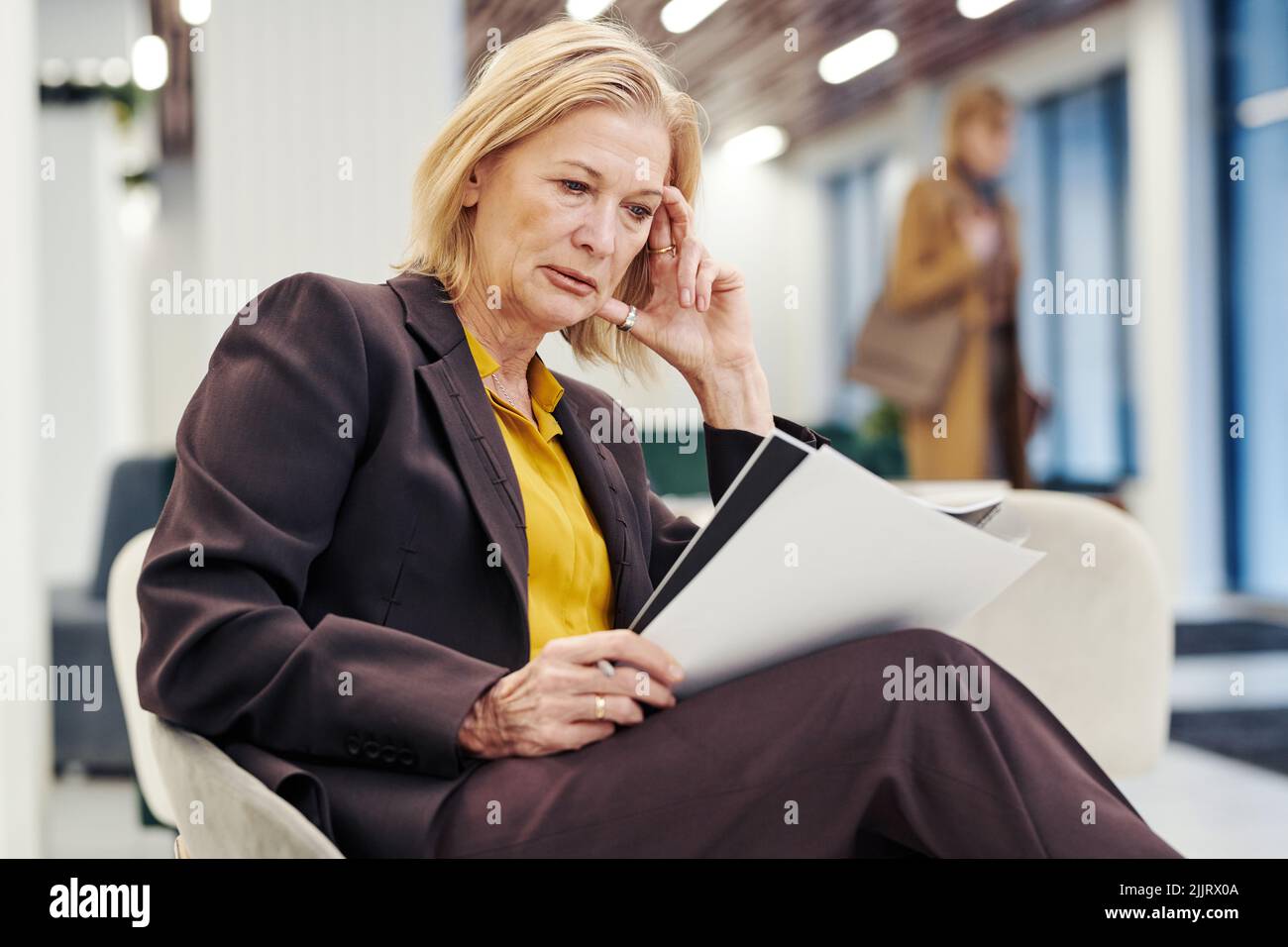 Serious female lawyer reading documents and preparing for the meeting while sitting on chair in the lobby of courthouse Stock Photo