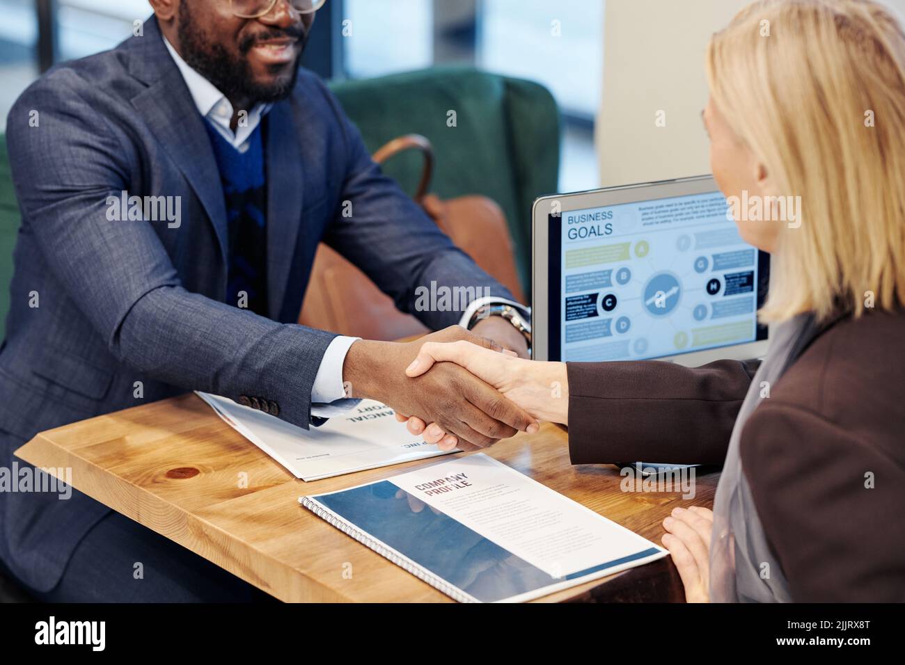 Close-up of business people sitting at the table and shaking hands, they concluding a deal during business meeting Stock Photo