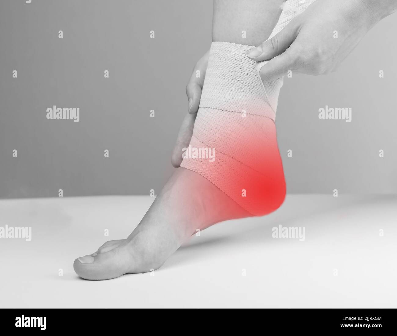 Woman wrapping elastic bandage around painful ankle to reduce heel pain and inflammation. Feet with red spot. Plantar fasciitis, tendinitis treatment. Health care concept. Black and white. photo Stock Photo