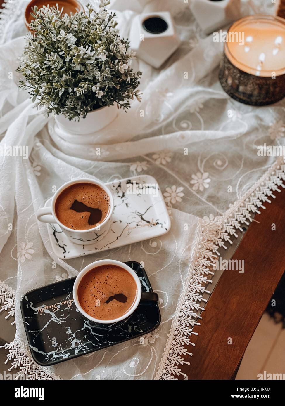A top view of beautifully arranged cups of coffee on a tablecloth decorated with flowers and candles Stock Photo