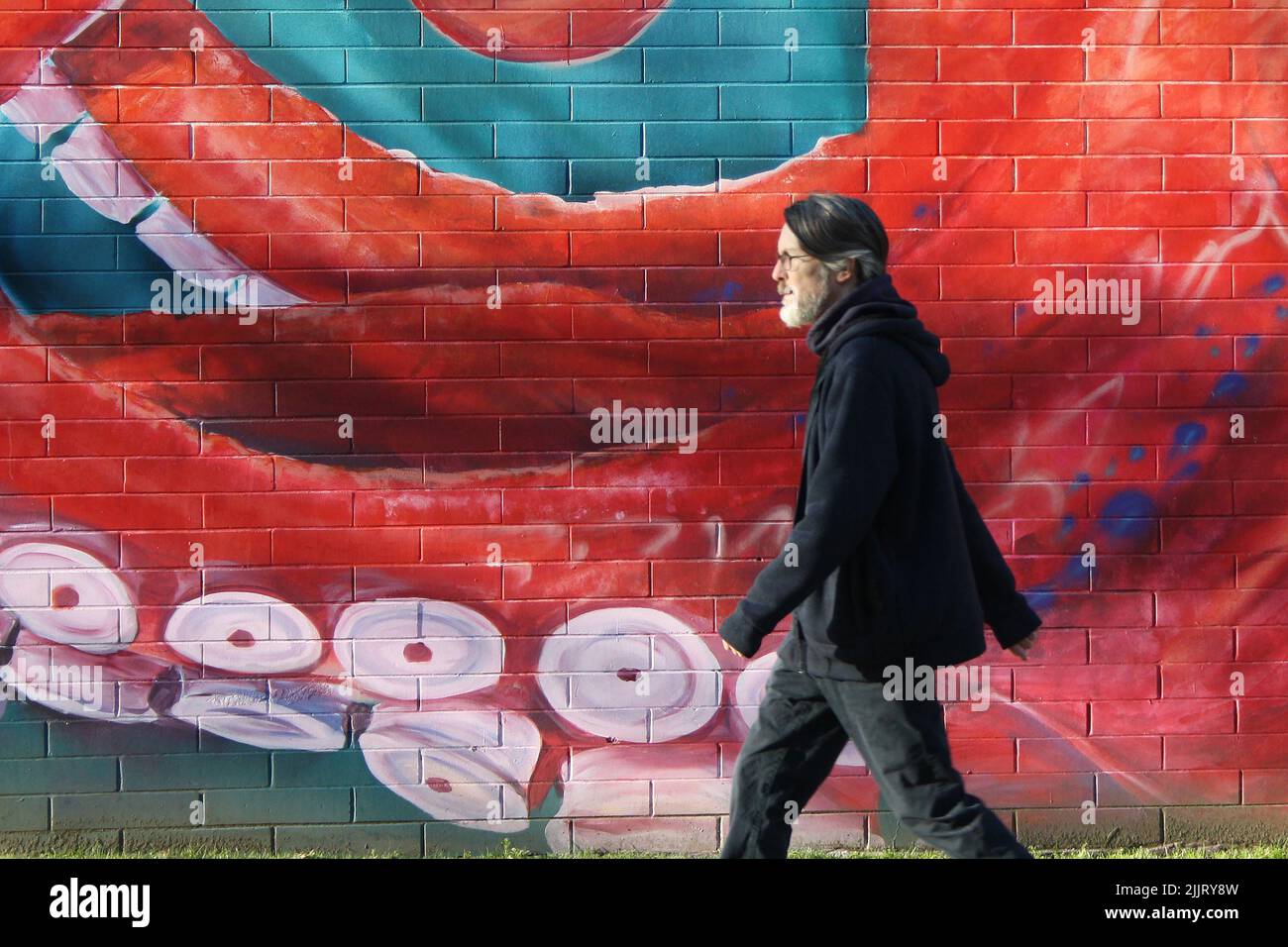 A Photo Of A Man In Black Walking Past Red Octopus Mural In Vancouver