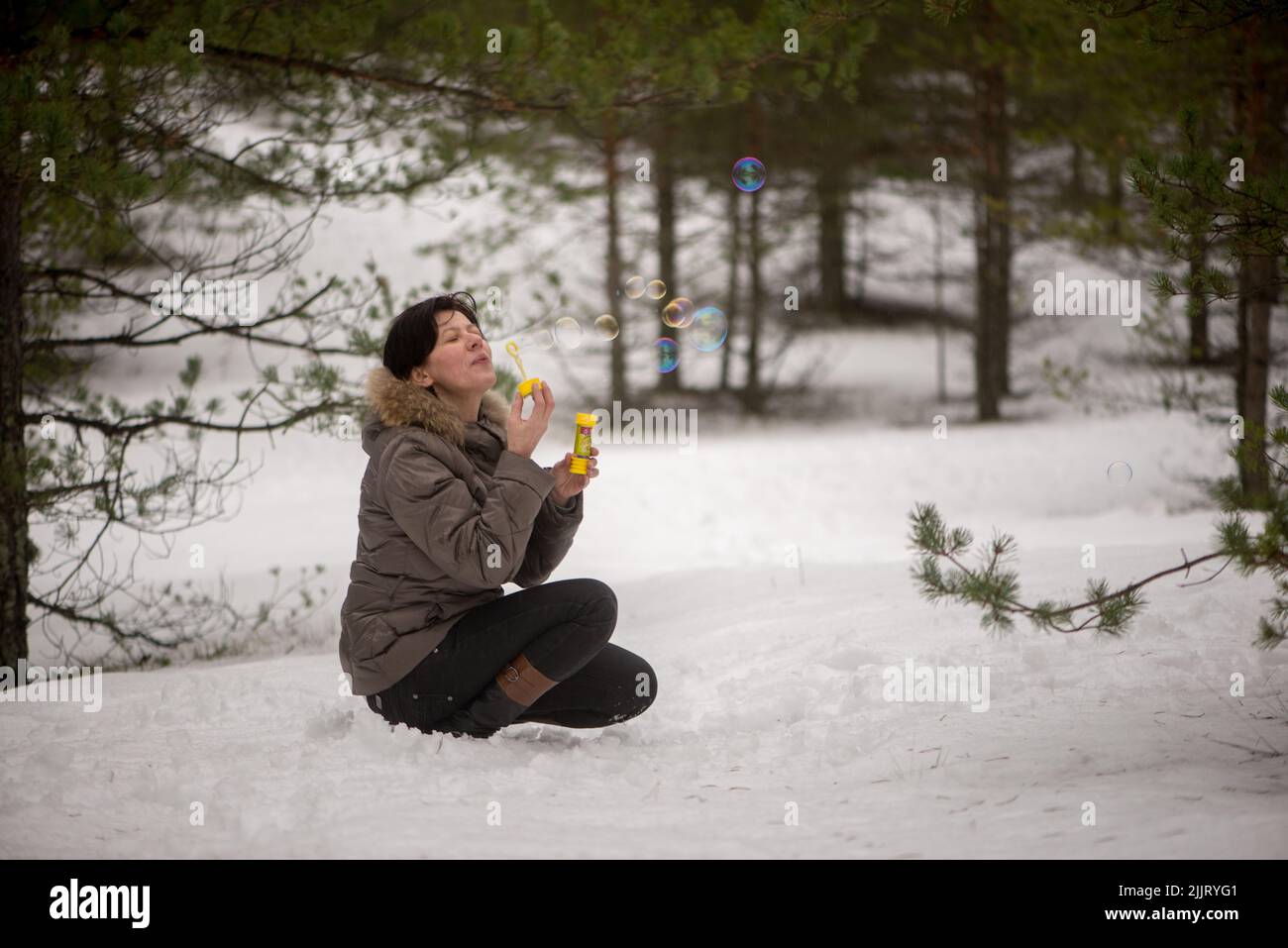 A Shallow focus of a Caucasian woman sitting and blowing bubbles in the snowy forest Stock Photo