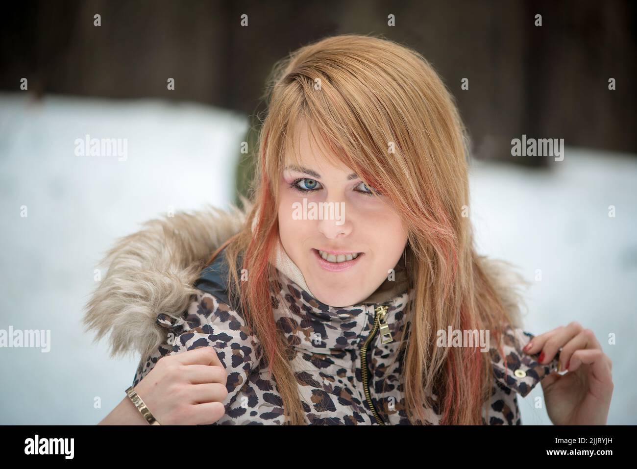 A portrait of a Caucasian blonde girl in a winter jacket with a blurred snoy background Stock Photo