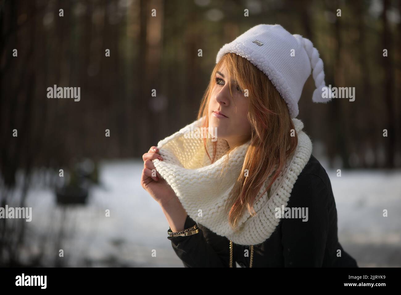 A Portrait of a Caucasian blonde girl wearing a white winter hat with a blurred snowy background Stock Photo