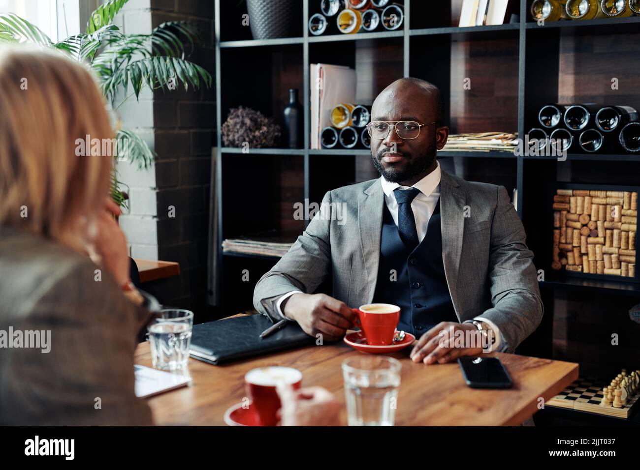 African businessman drinking coffee and talking to his colleague during coffee break at the restaurant Stock Photo