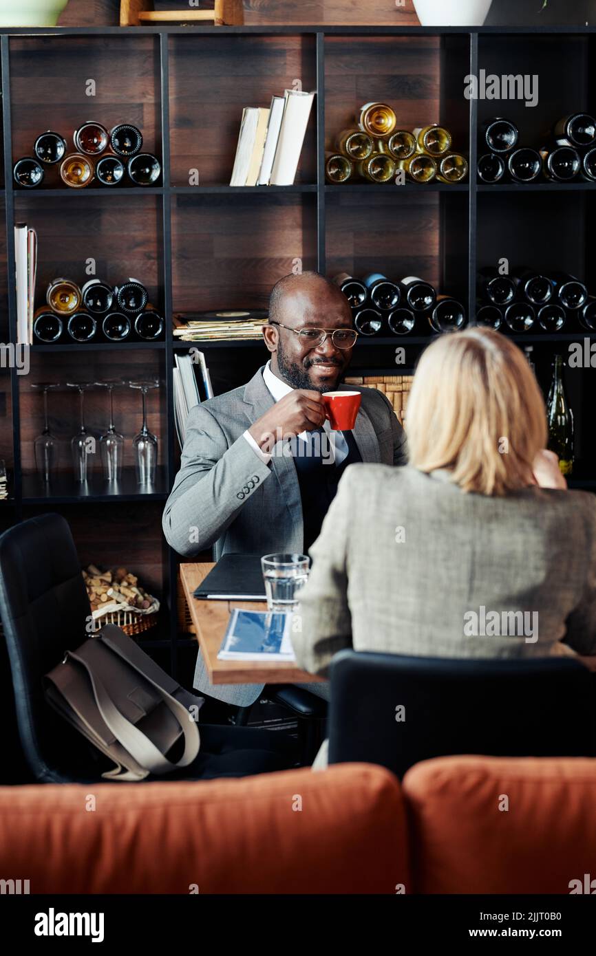 African businessman drinking coffee and smiling to his partner during conversation at the