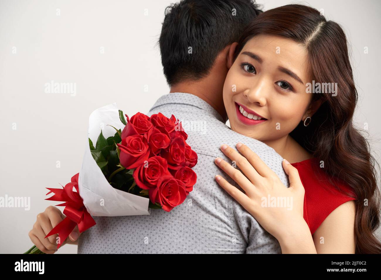 Adorable Asian woman looking at camera with deep gray eyes while embracing her soulmate, isolated on white background Stock Photo