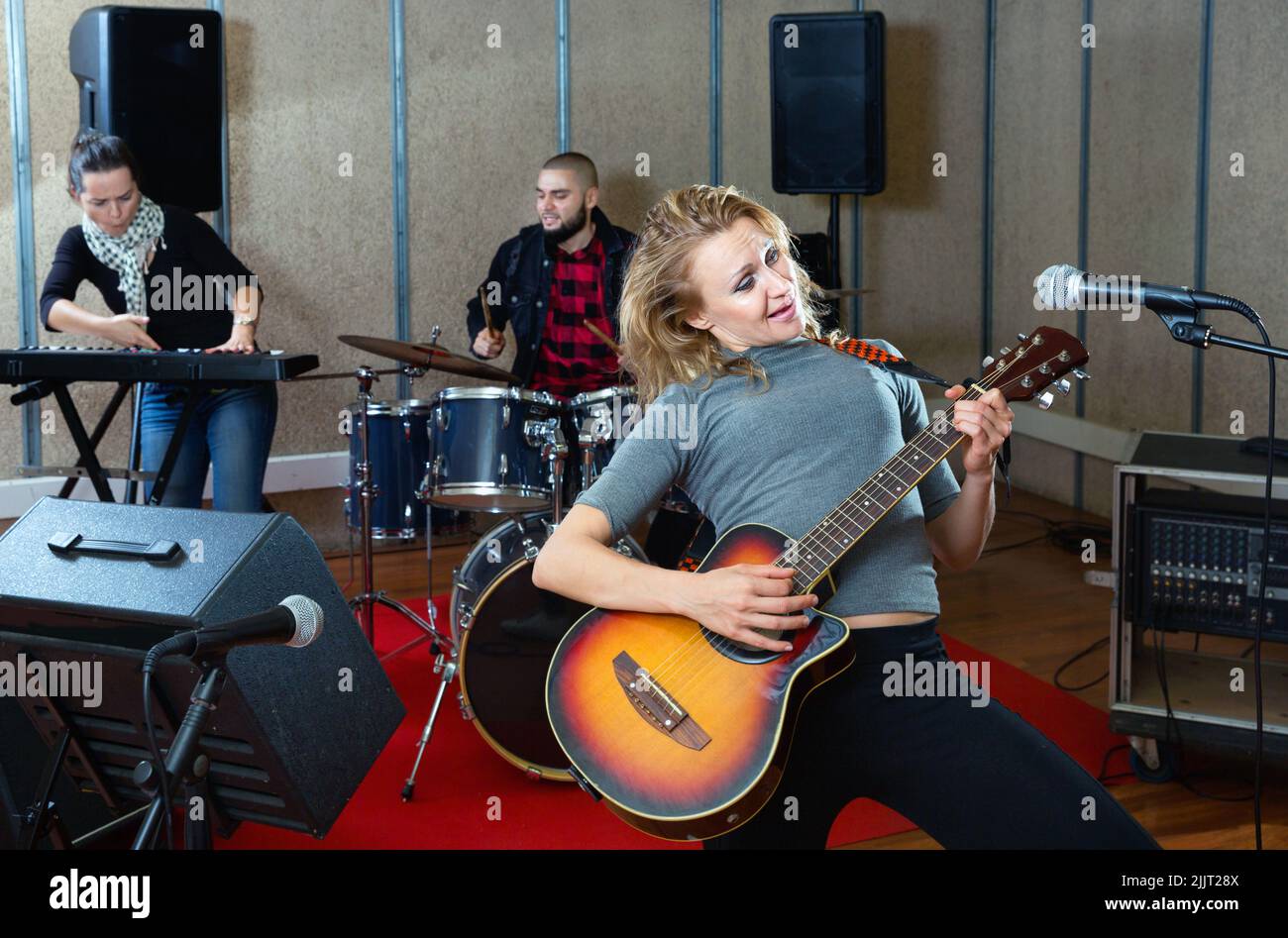 Attractive female soloist playing guitar and singing with her music band in sound studio Stock Photo
