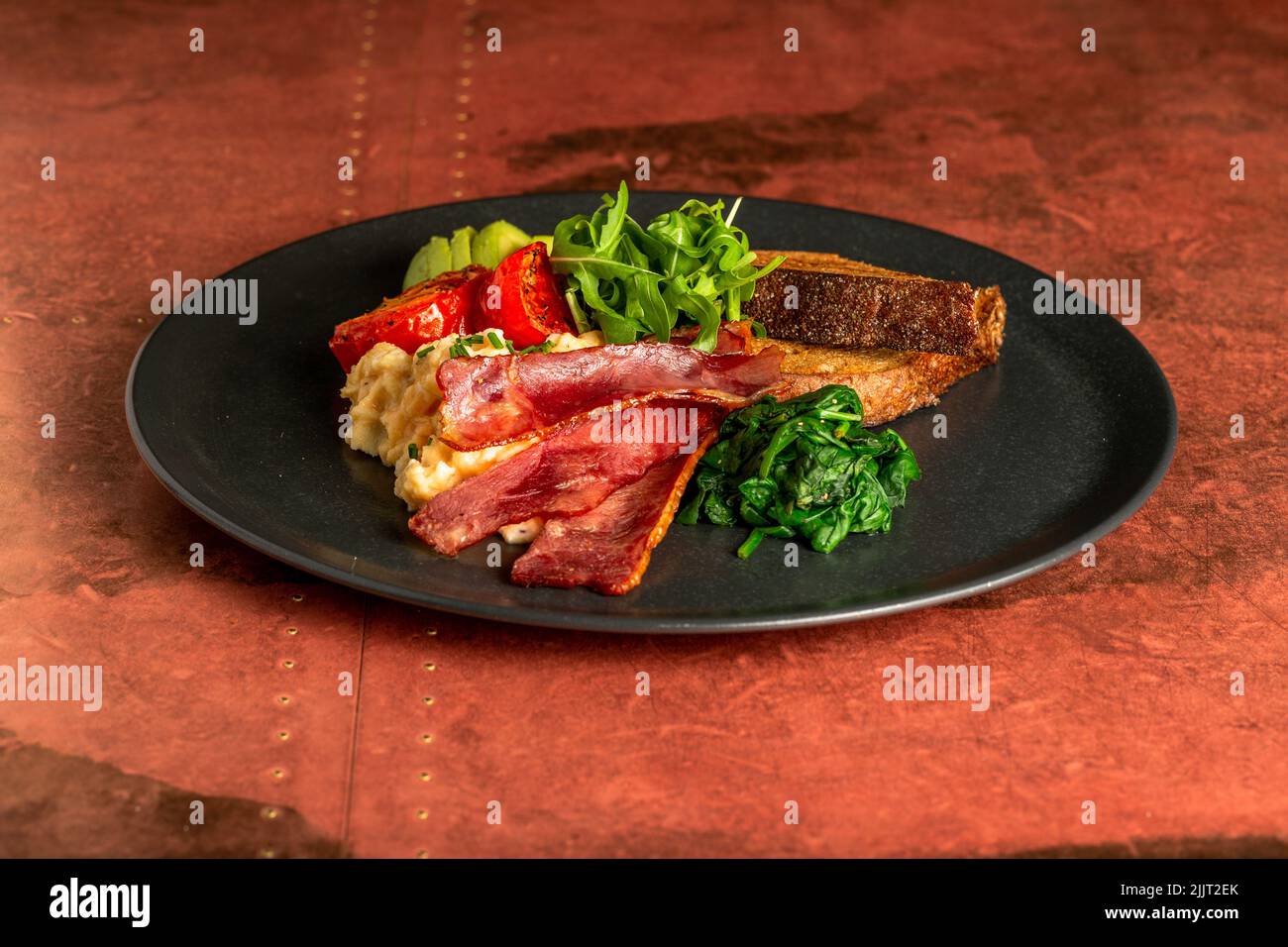 An appetizing breakfast with fried bacon, tomato, avocado, bread and some greens Stock Photo