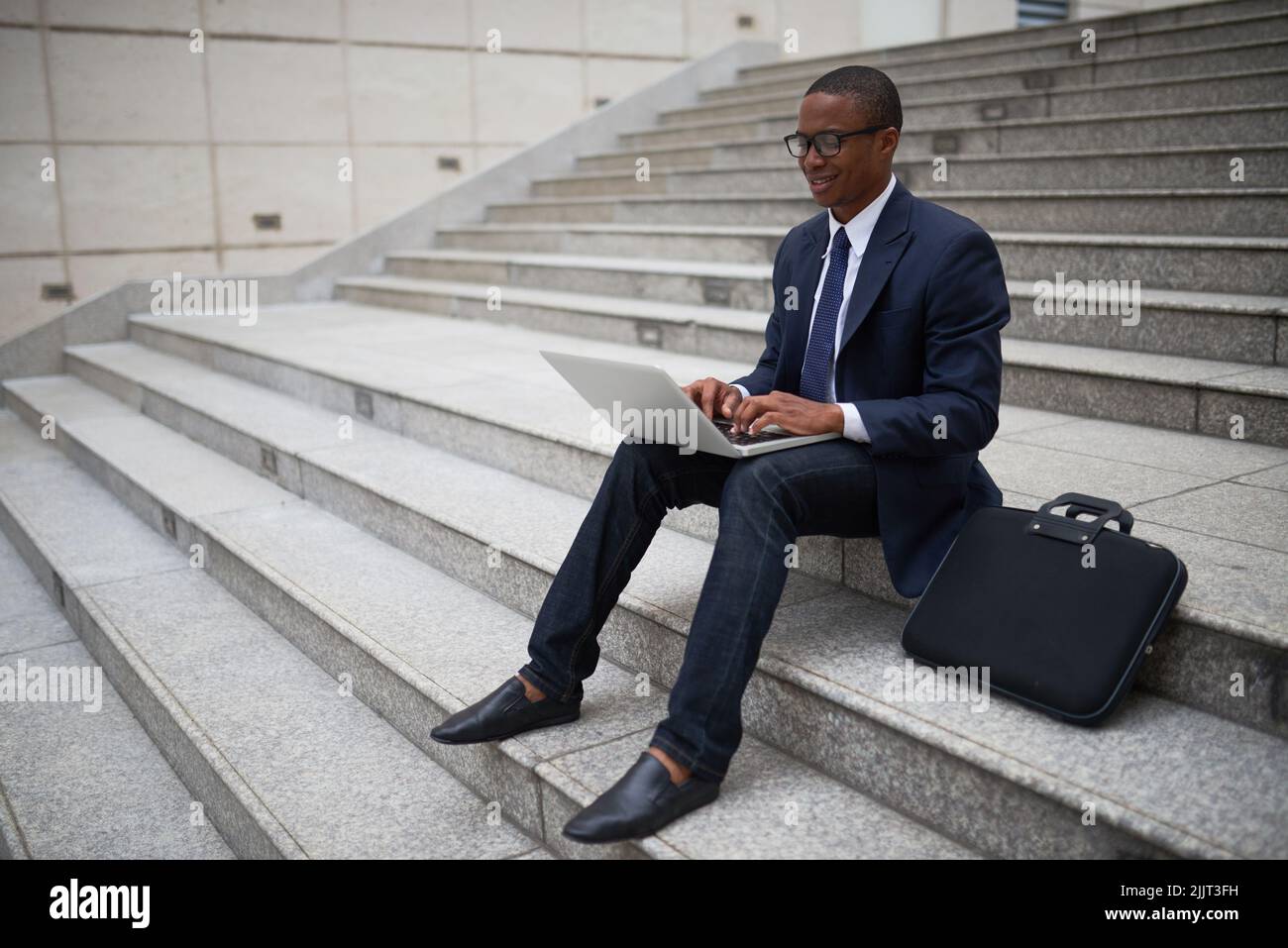 Smiling young businessman sitting on steps and working on laptop Stock Photo