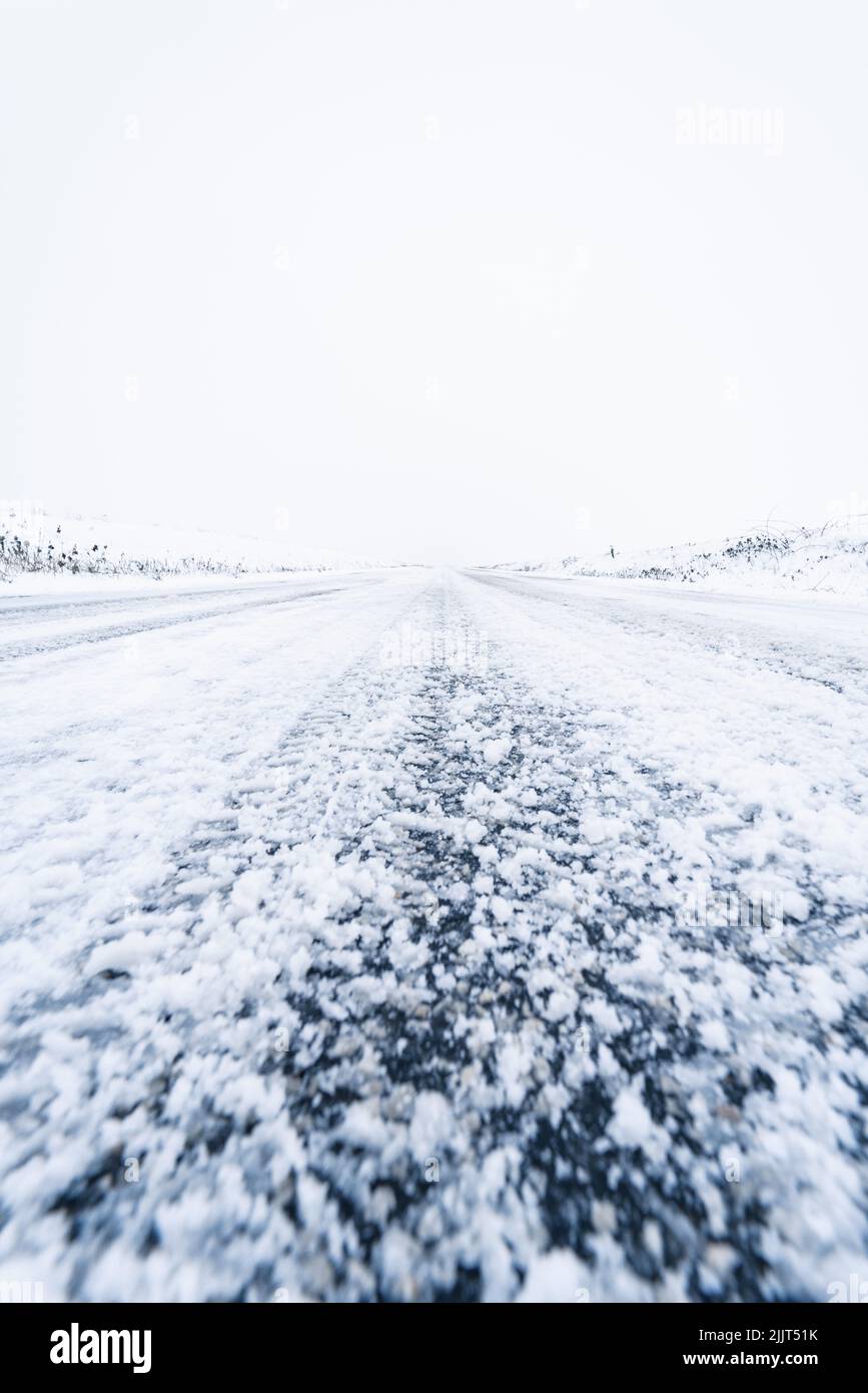 A vertical vanishing point shot of a snowy countryside road Stock Photo