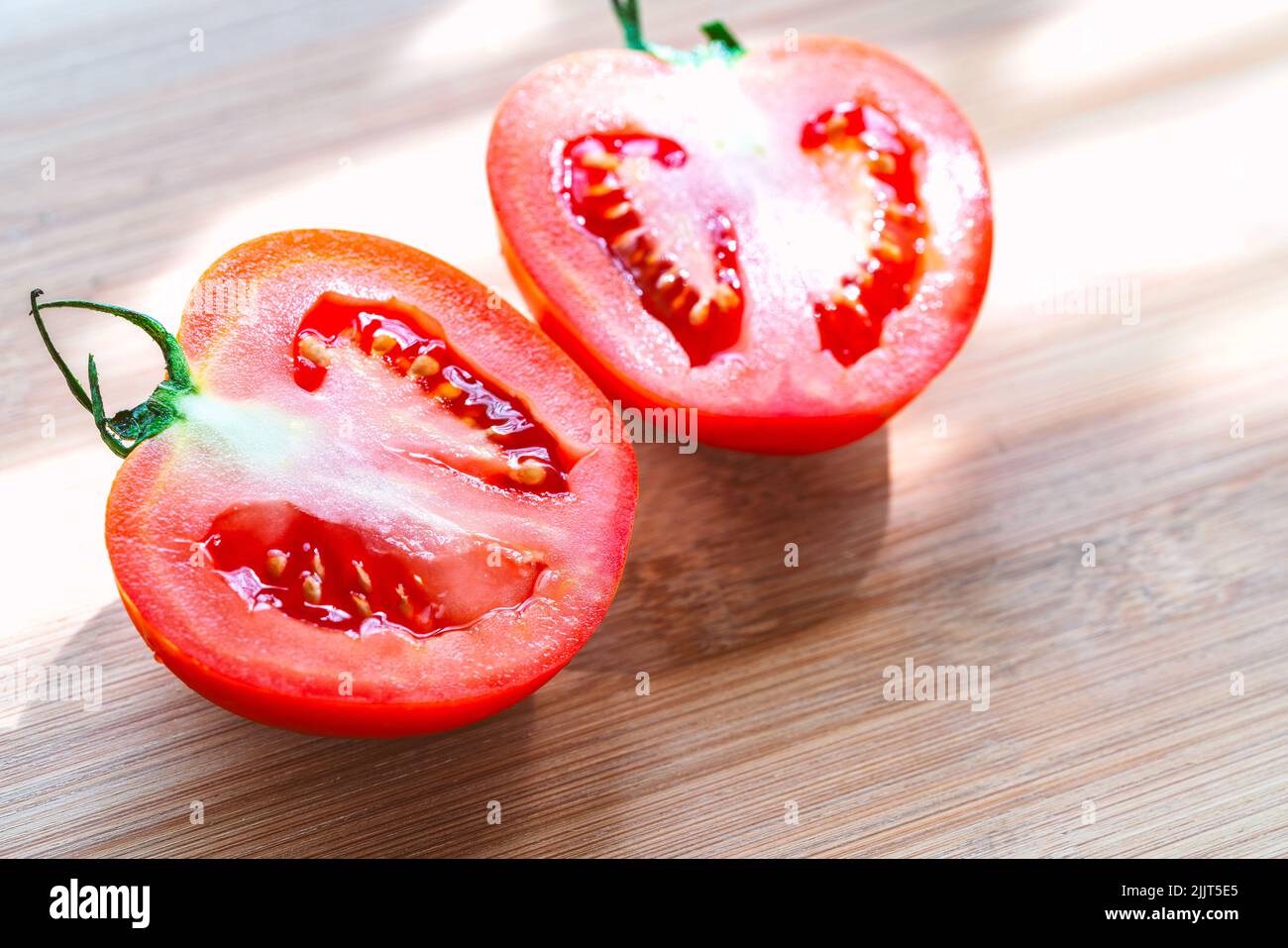 Close up cut-half of two red juicy tomatoes on wooden cutting board, fresh two half-cut tomatoes with natural light. Stock Photo