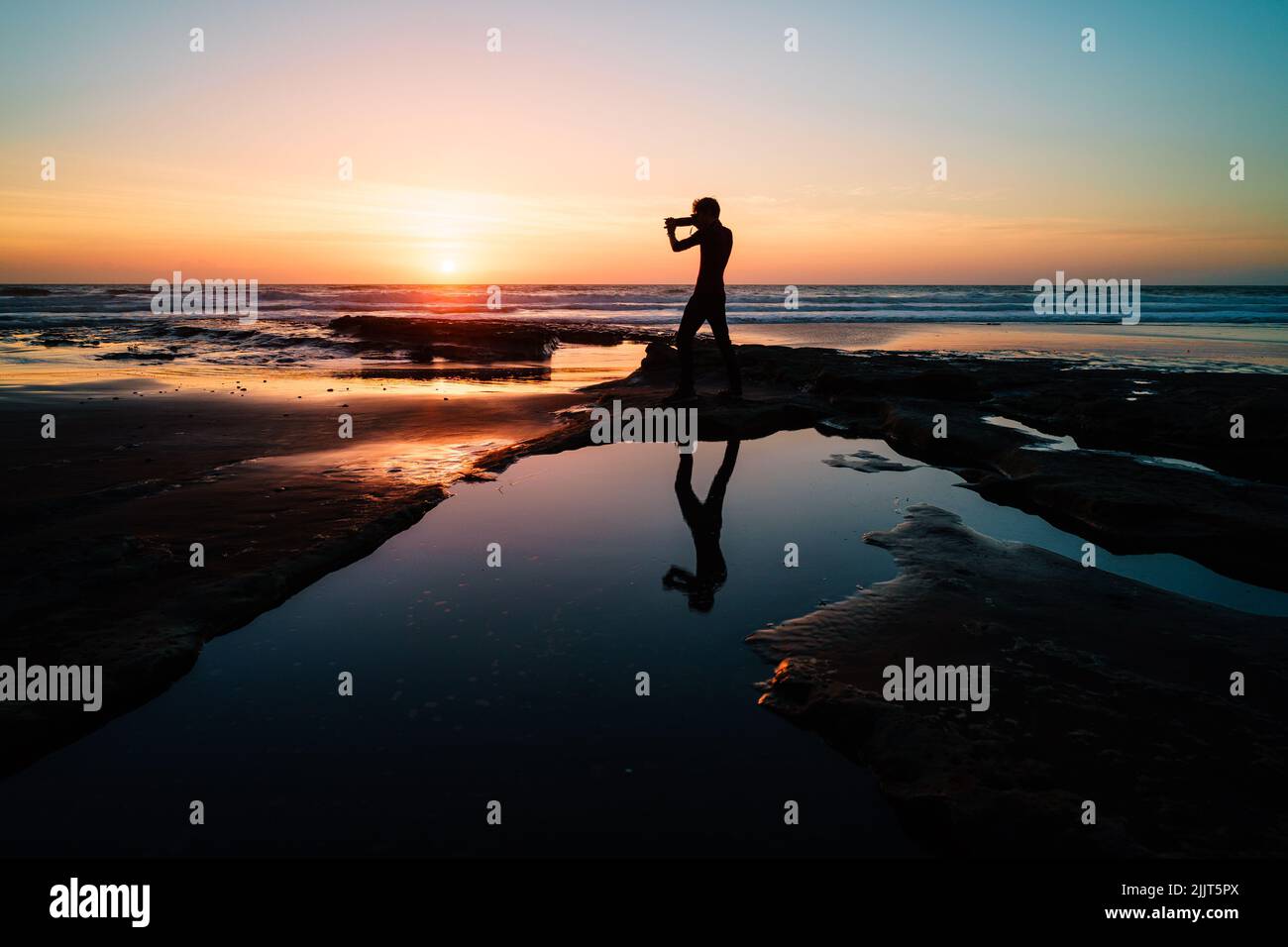 A silllhouette of a man with a photo camera at Waiiti Beach in New Zealand at sunset Stock Photo