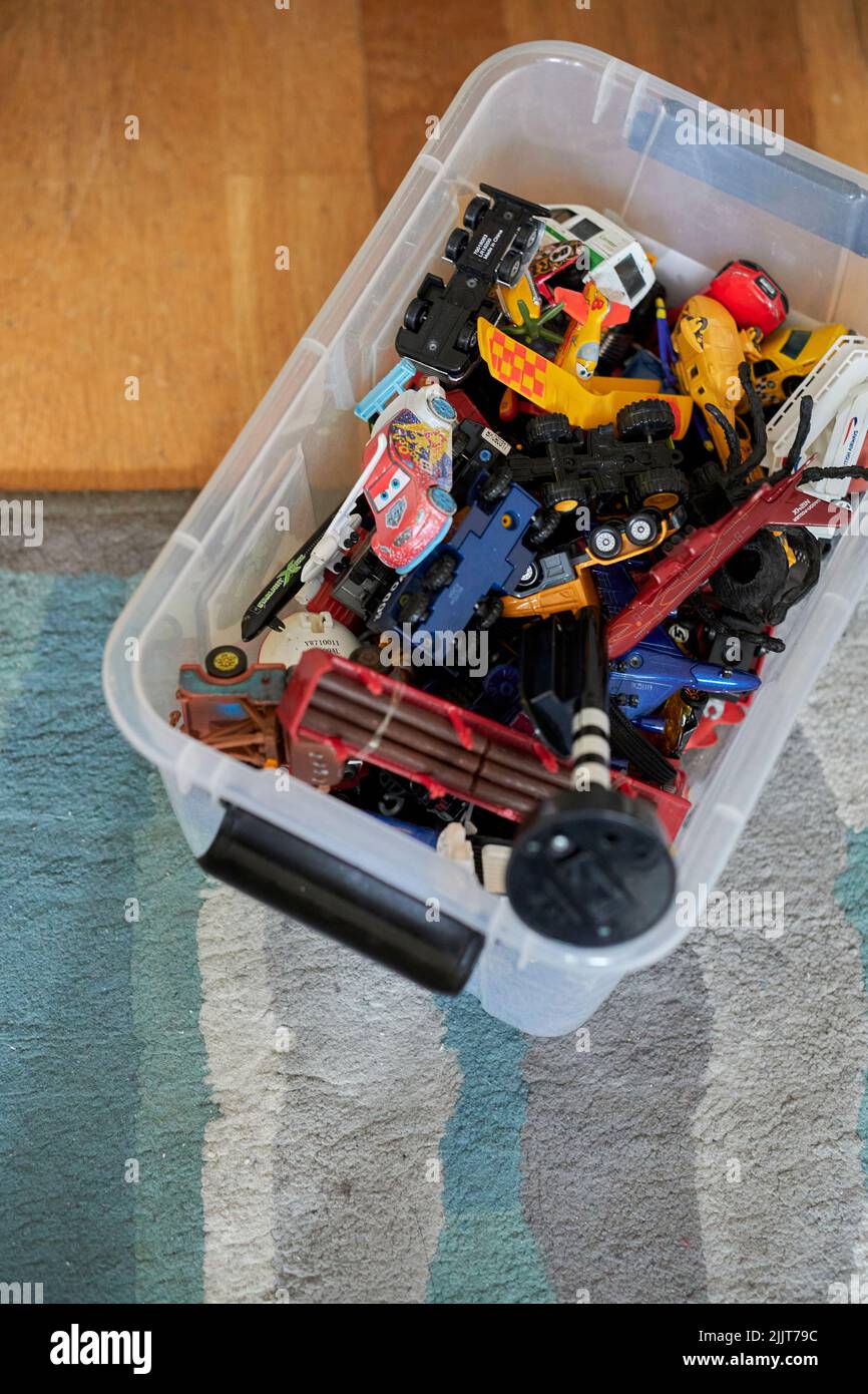A plastic container filled with toy model vehicles and planes on a carpet floor Stock Photo