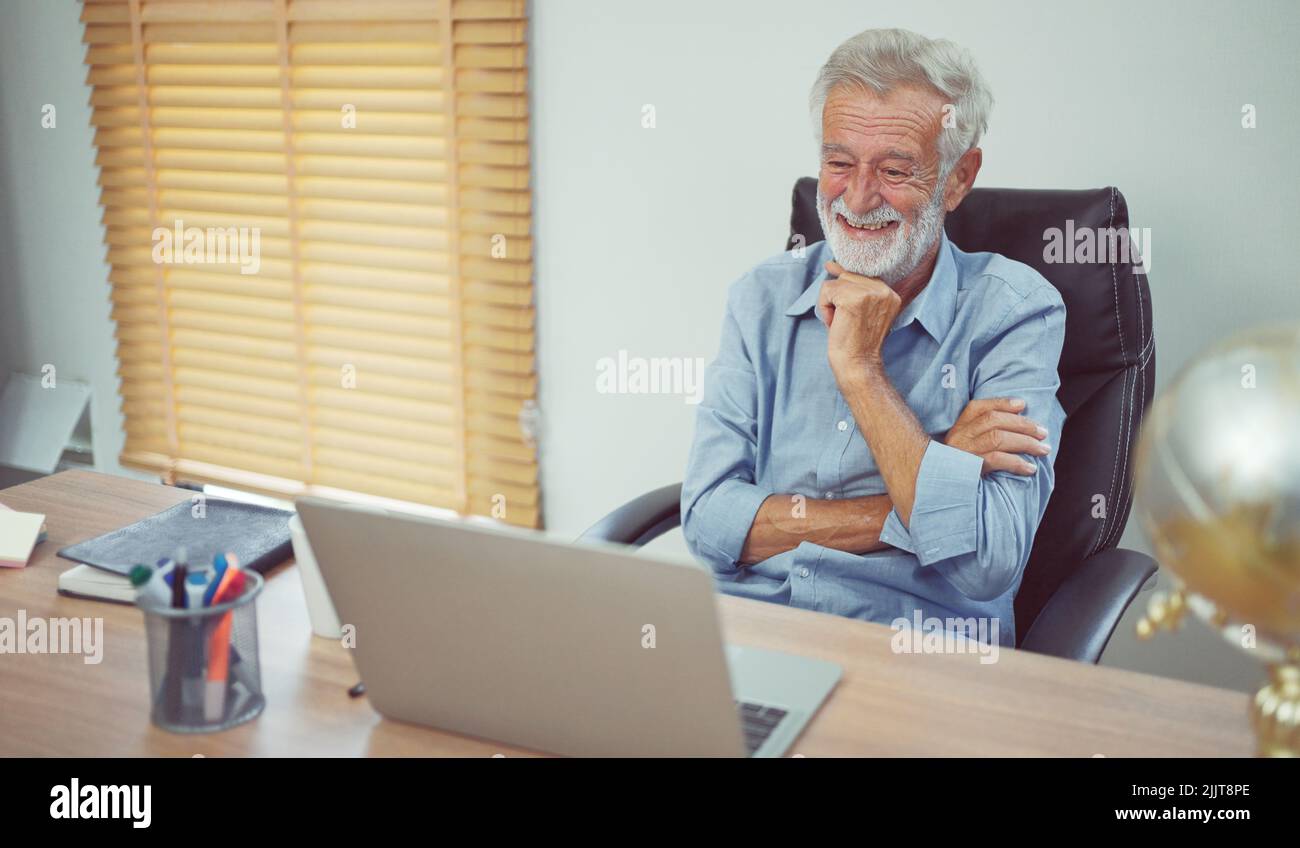 Happy senior older man using laptop computer at work desk. Stock Photo