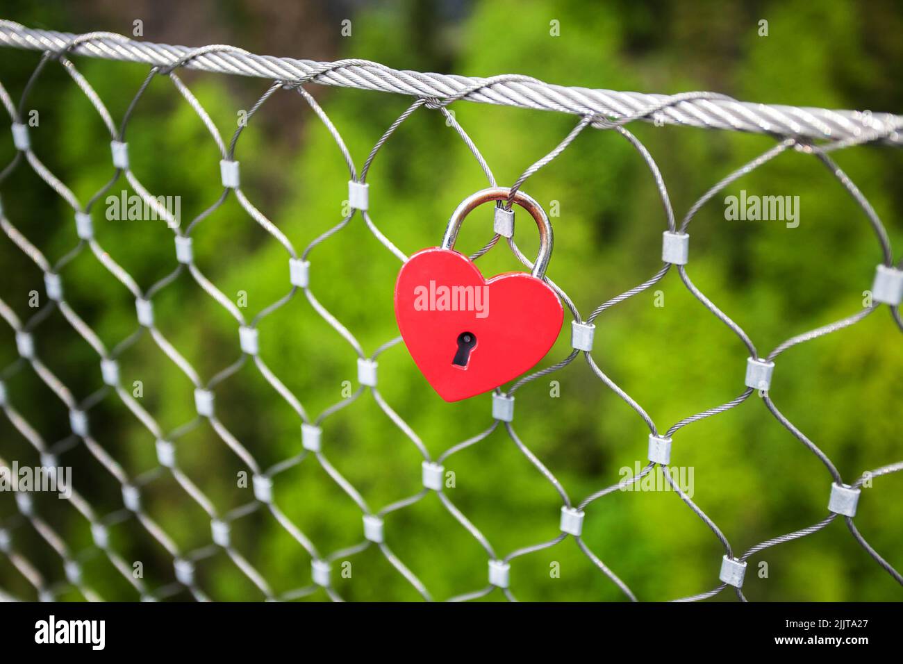 A closeup of red lock in heart shape hanging from metal fence Stock