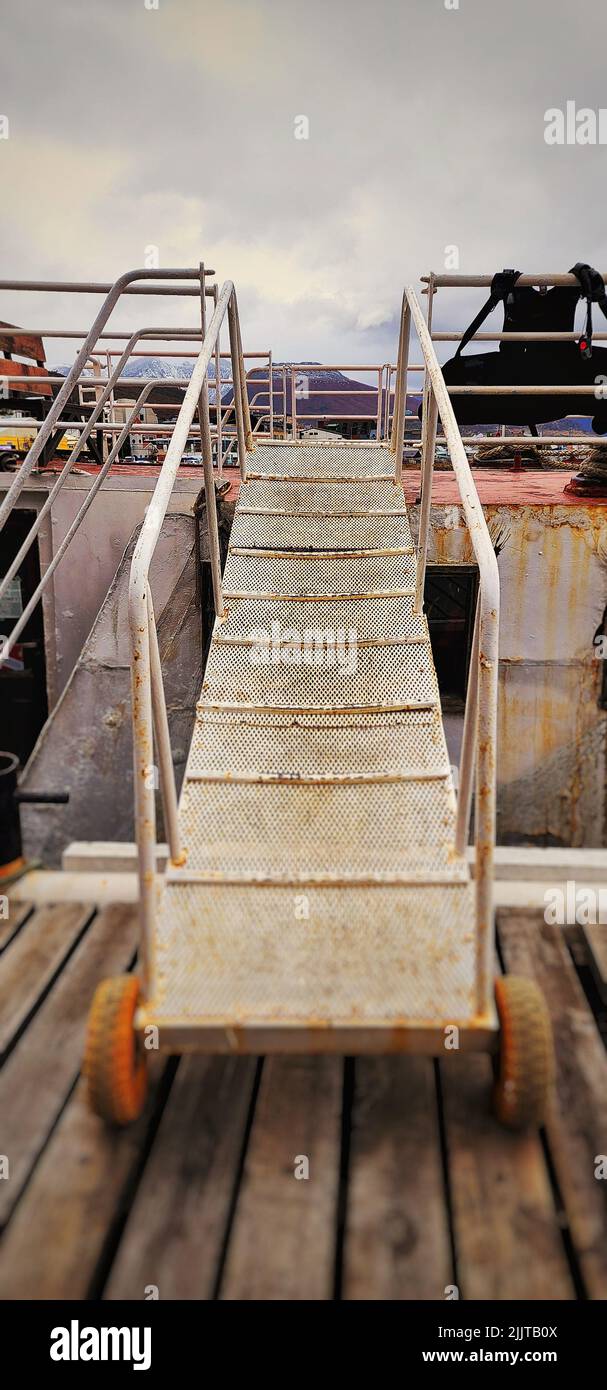 A vertical shot of rusty metallic stairs leading to an old vessel under a cloudy sky Stock Photo