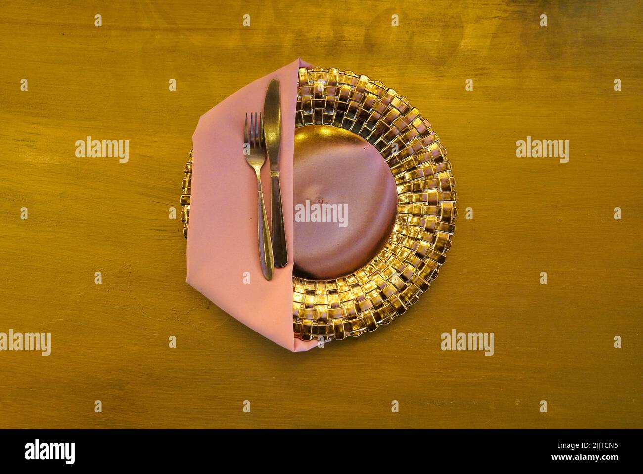 A top view of a golden plate with pink napkins and golden cutlery for a