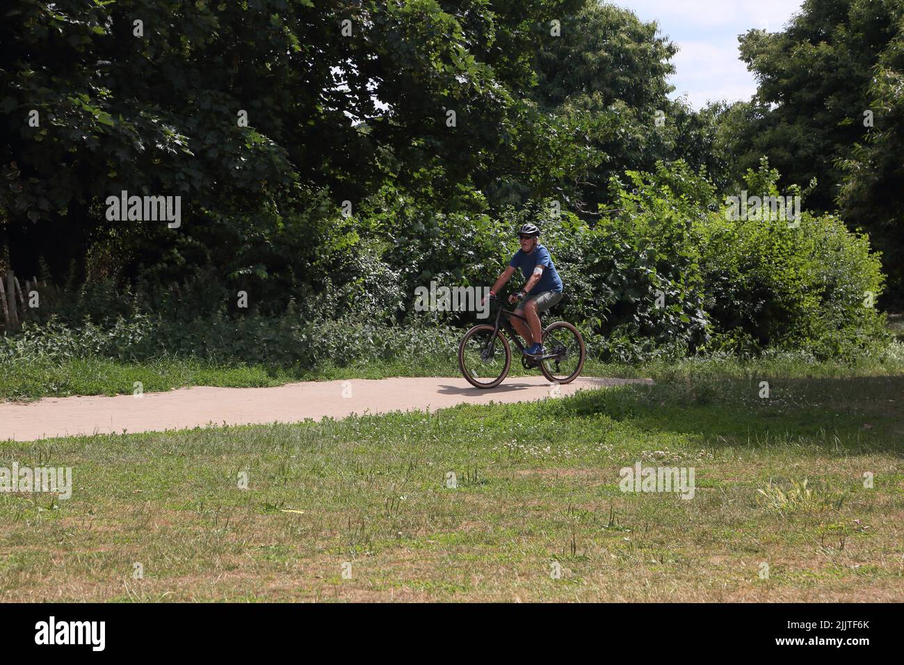 Man in his Seventies Riding Bicycle through Nonsuch Park Surrey England Stock Photo