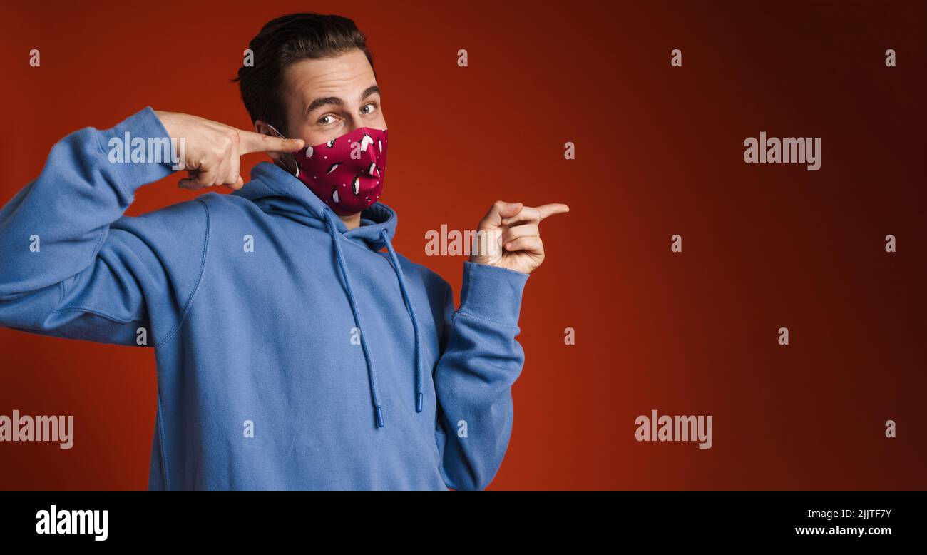 Young excited man wearing face mask pointing fingers aside isolated over red background Stock Photo